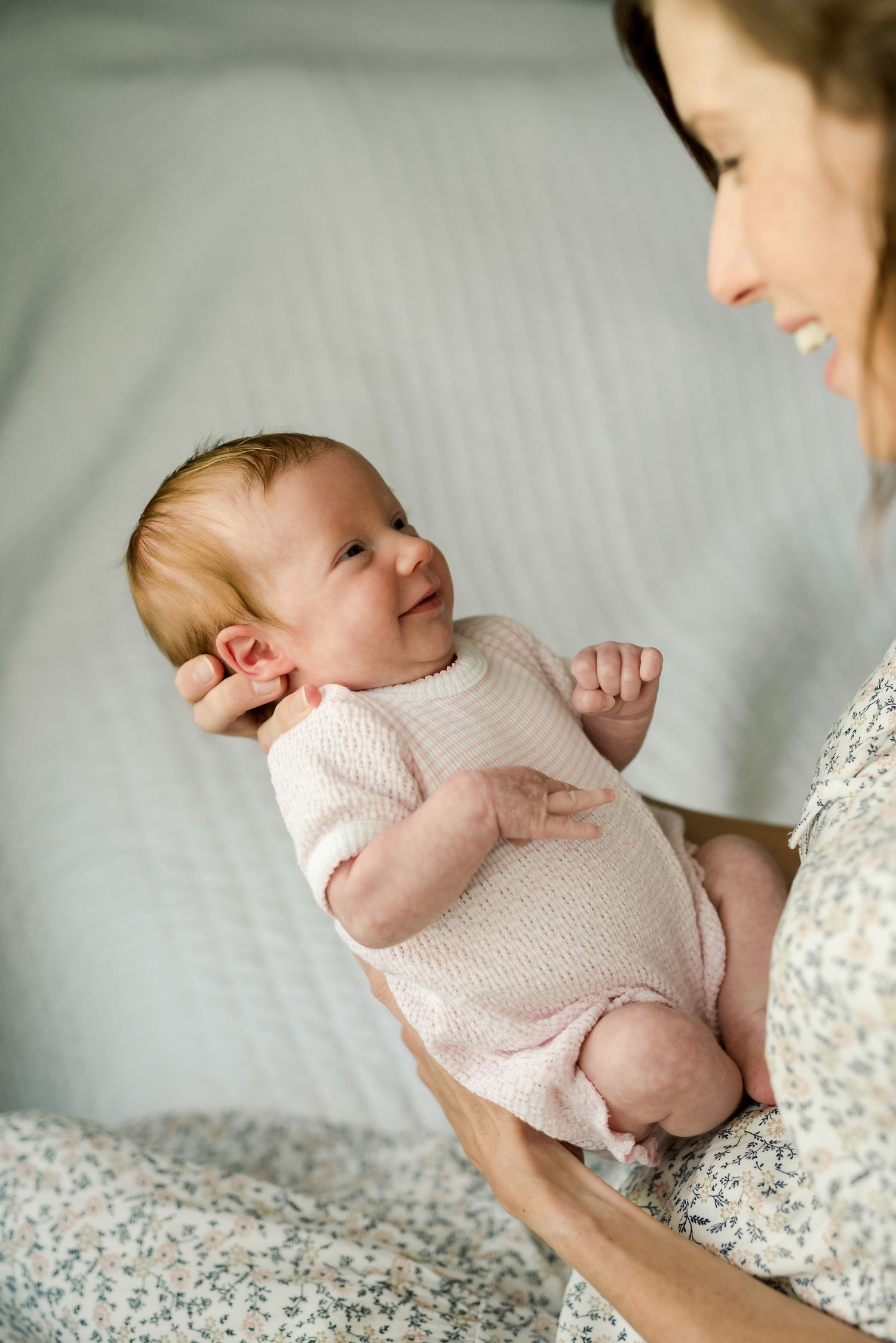Tender moment between mother and smiling baby on white bedding.