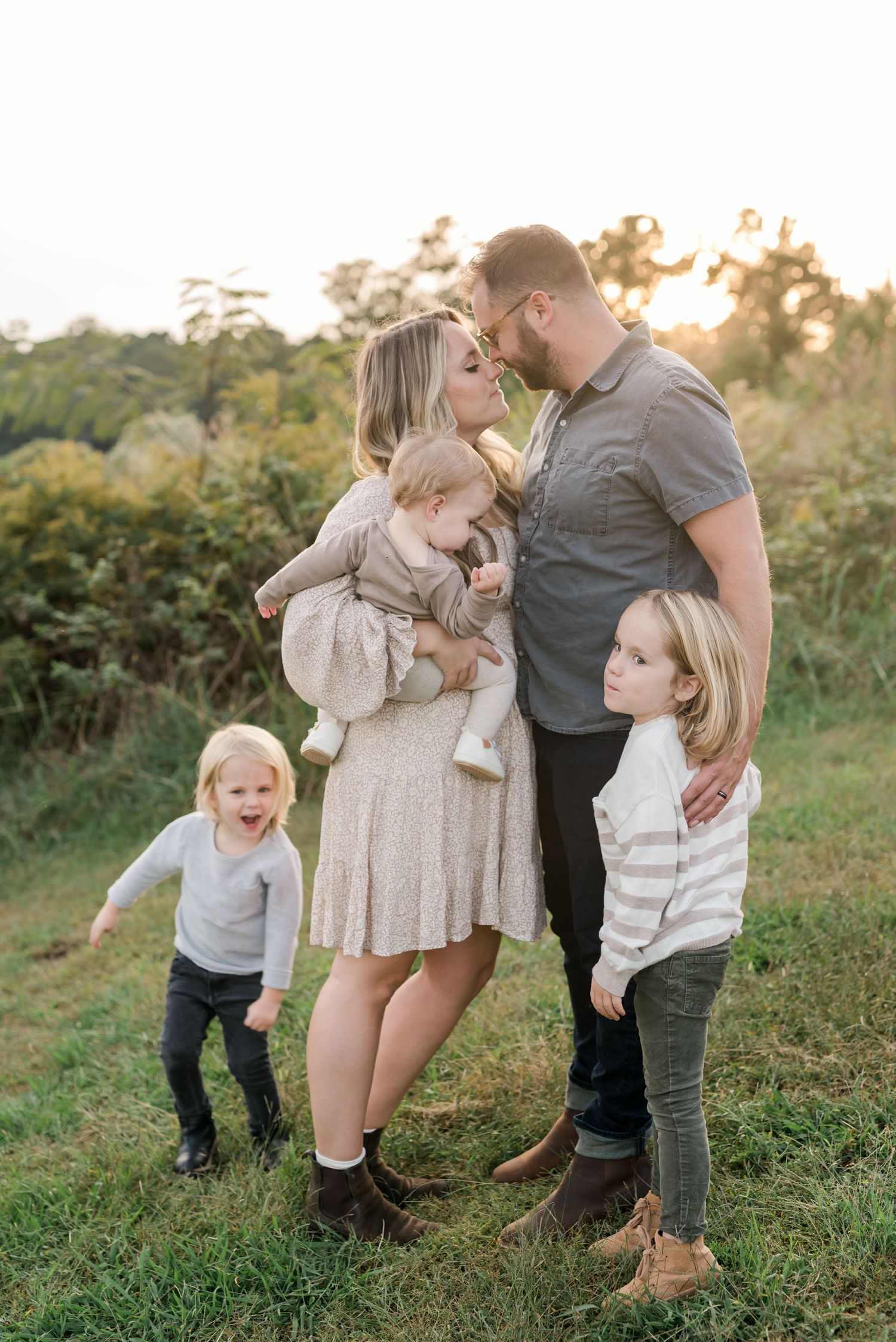 A family shares an intimate moment together in a sun-lit field at golden hour.