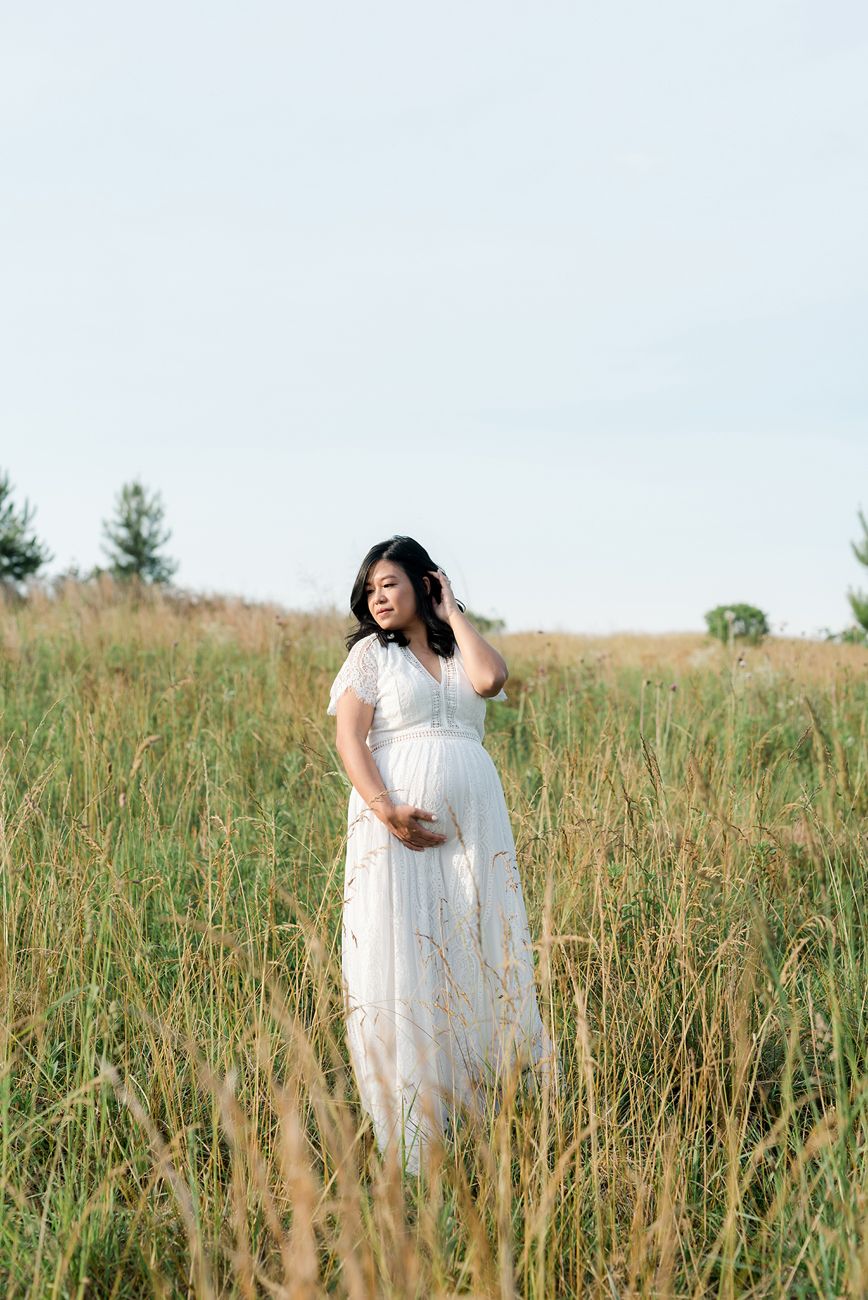 Maternity session in a golden field with flowing white dress and natural sunlight.
