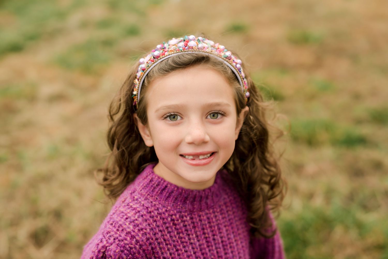 Person in purple sweater with curly hair wearing floral headband smiling at camera.