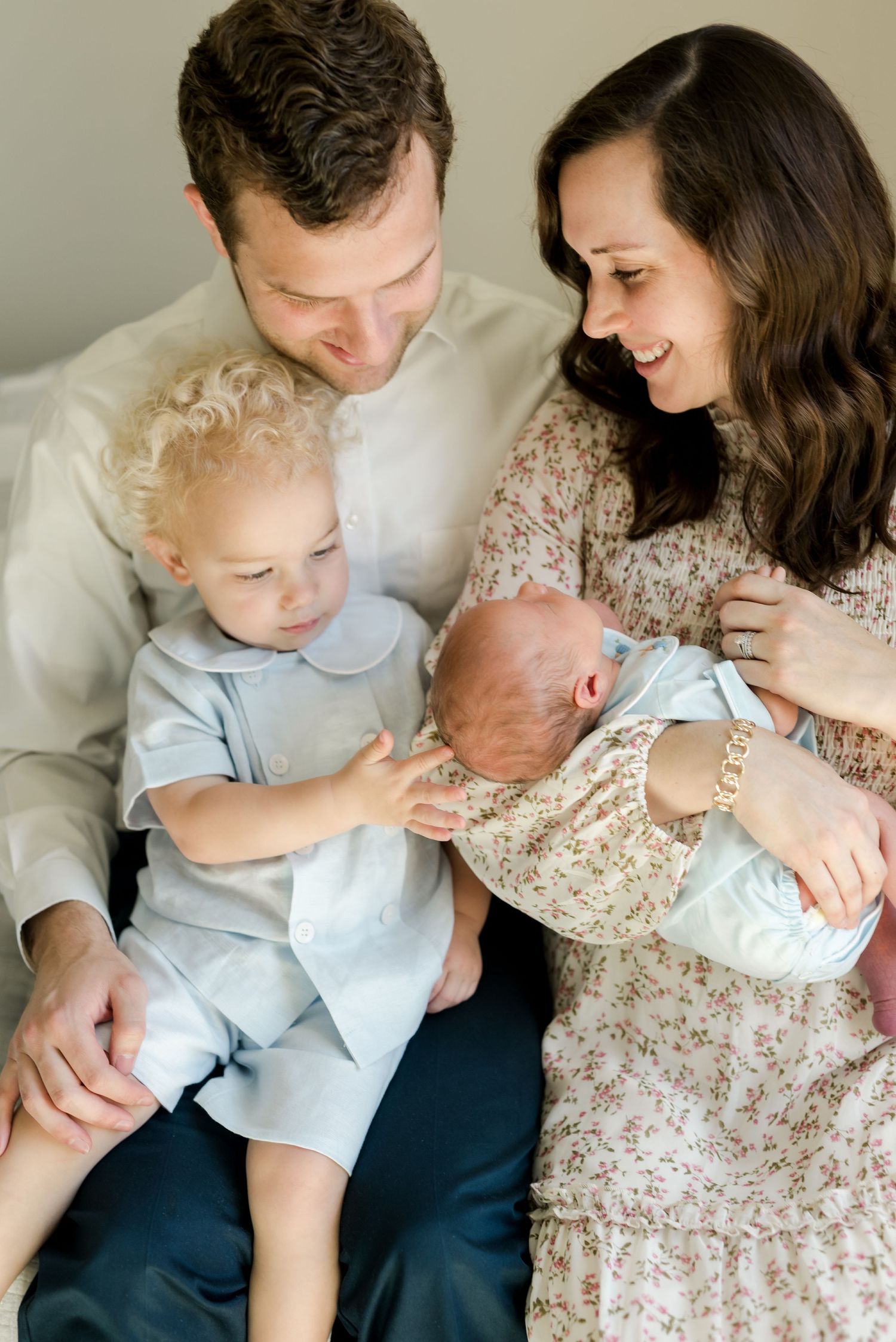 Sweet family moment as toddler gently touches newborn sibling while parents look on lovingly.