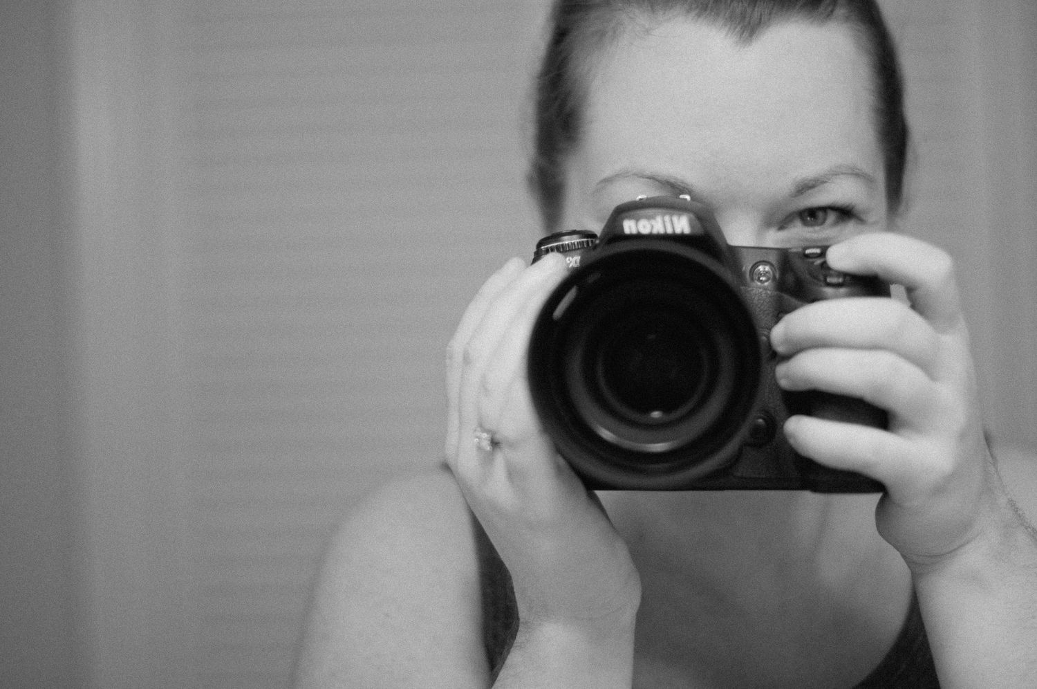 Person taking self-portrait with professional DSLR camera in black and white.