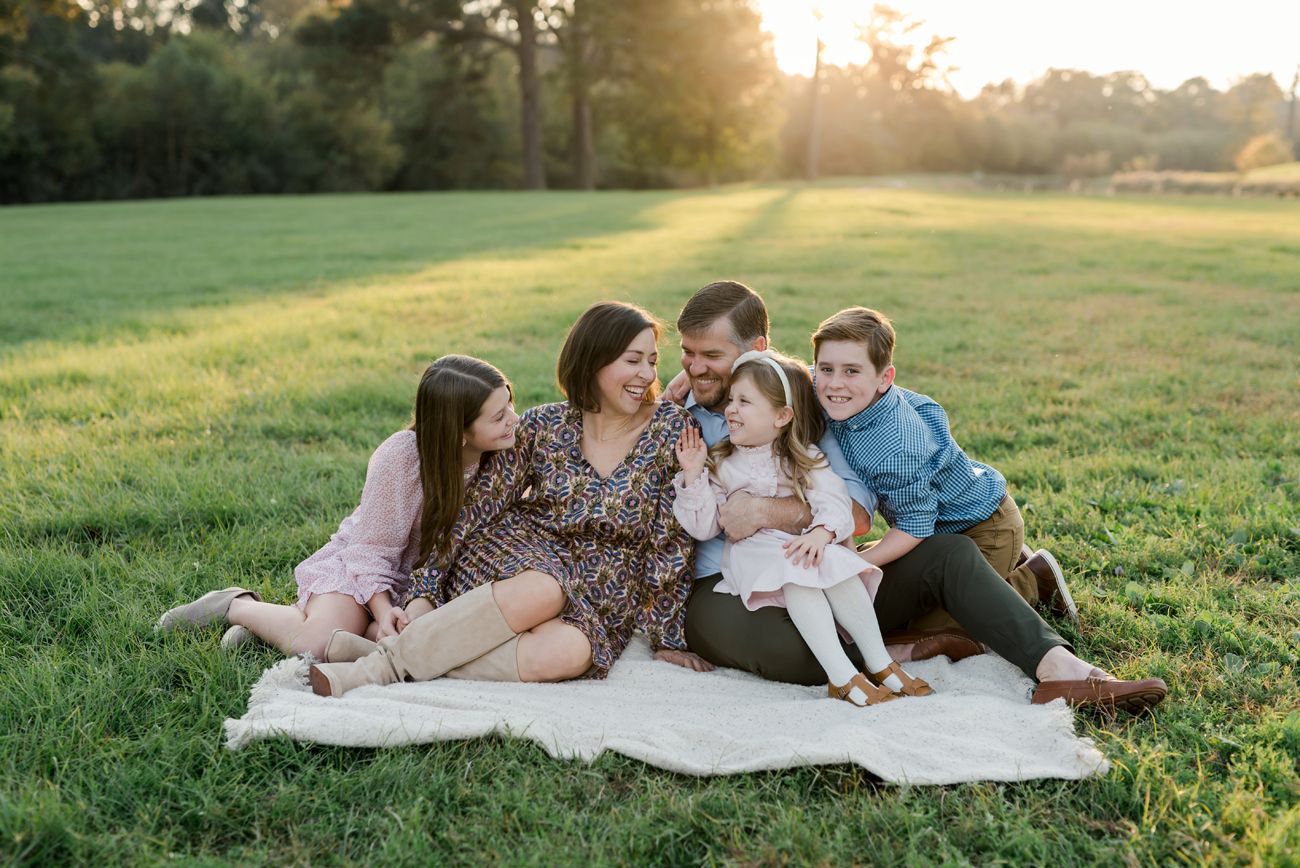 Family relaxing together on blanket in grassy field during golden hour sunset.