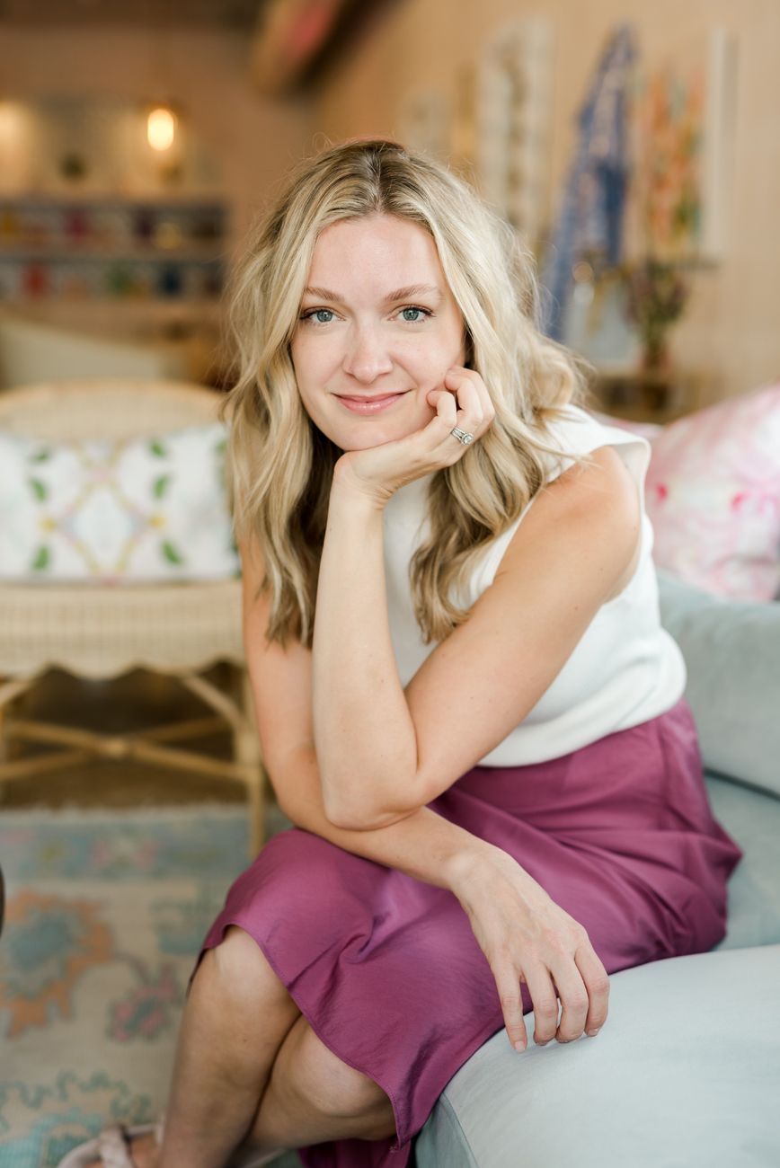 Woman in white top and pink skirt sitting on couch in stylish interior.