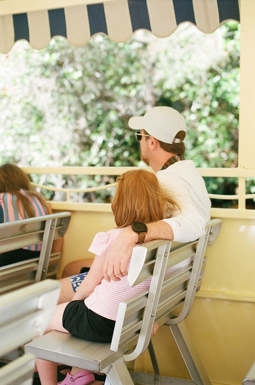 Passengers riding on a shaded attraction bench at Disney theme park.