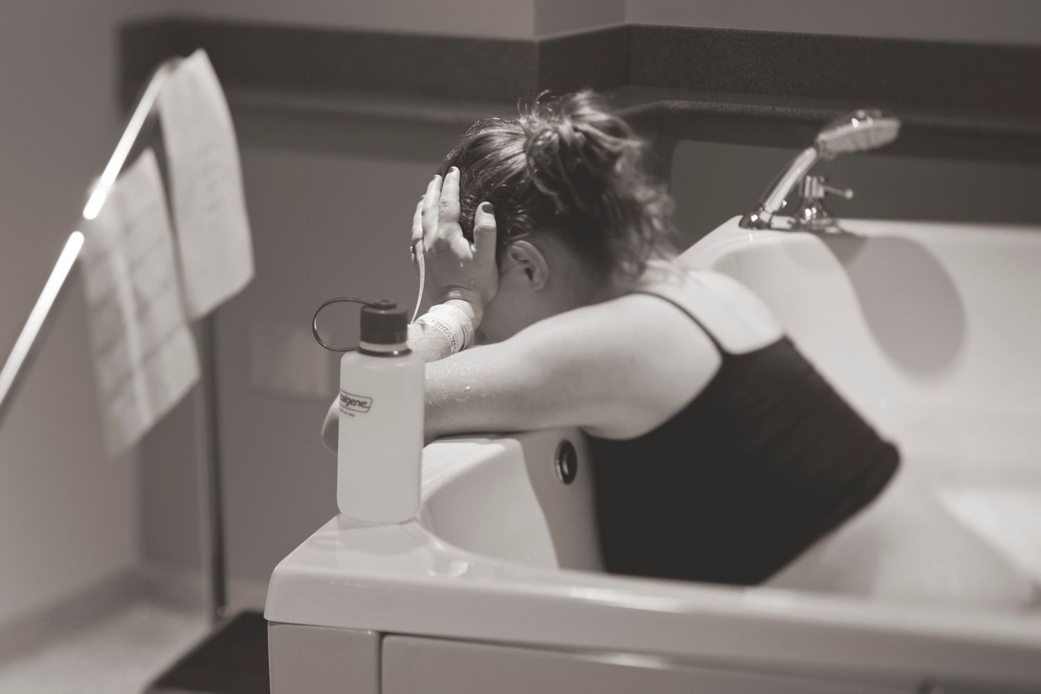 Black and white photo of someone leaning over sink in medical facility.