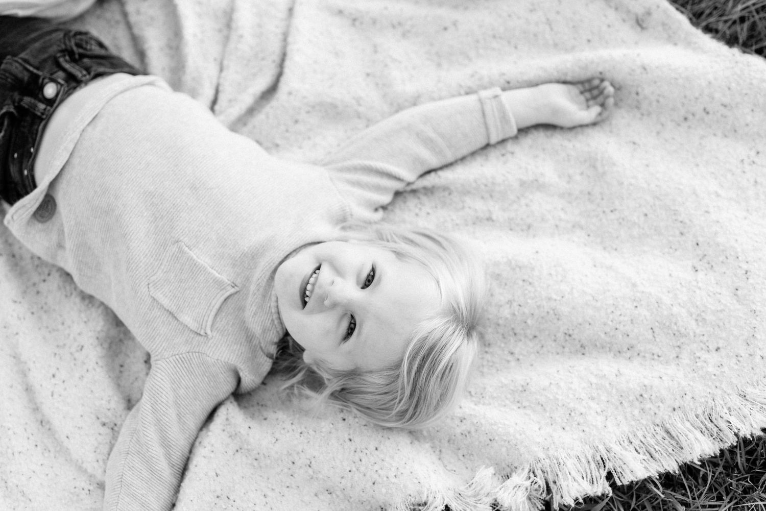 Black and white portrait of child laying on blanket with joyful expression.
