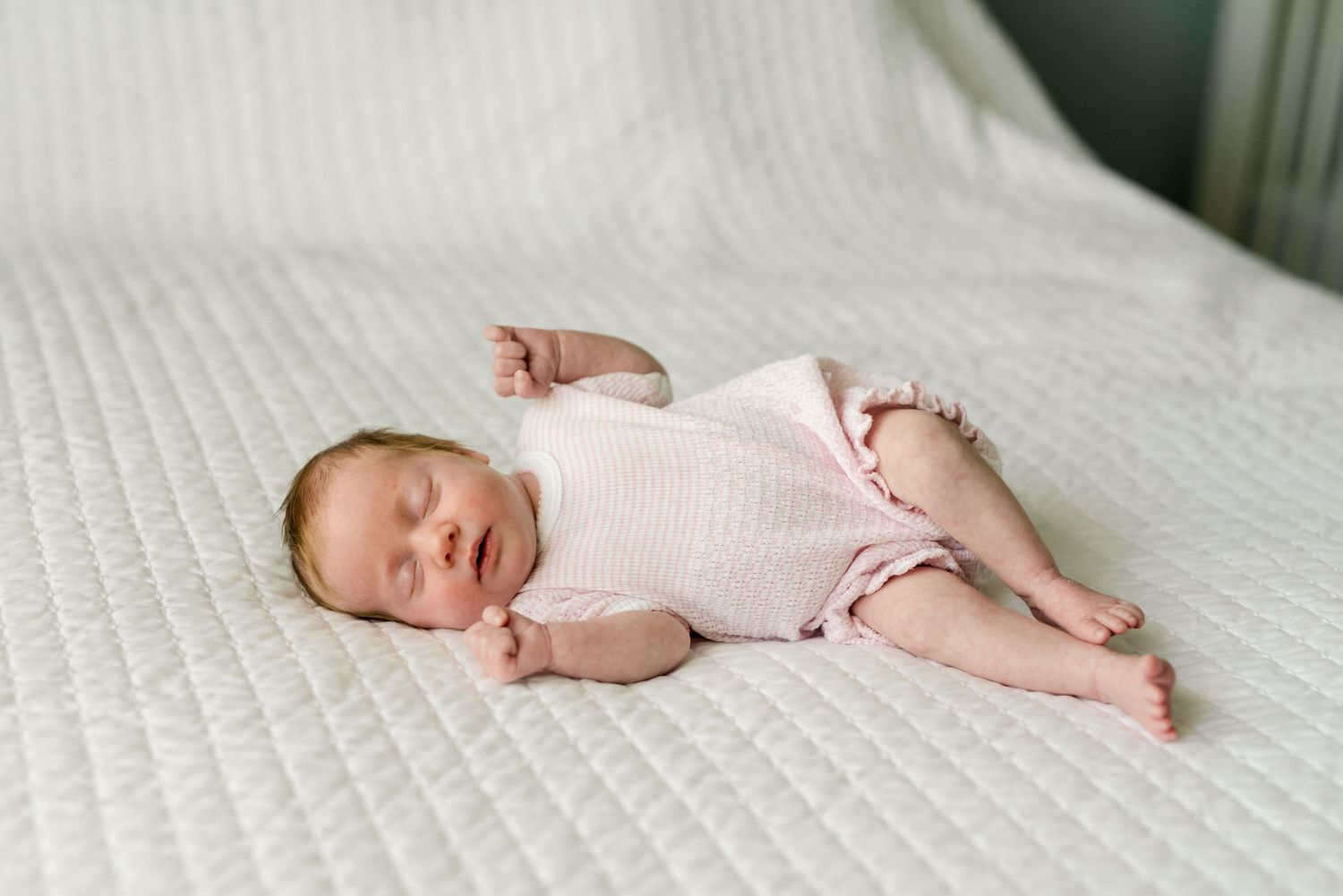Sleeping newborn in pink outfit lying on white textured bedding.