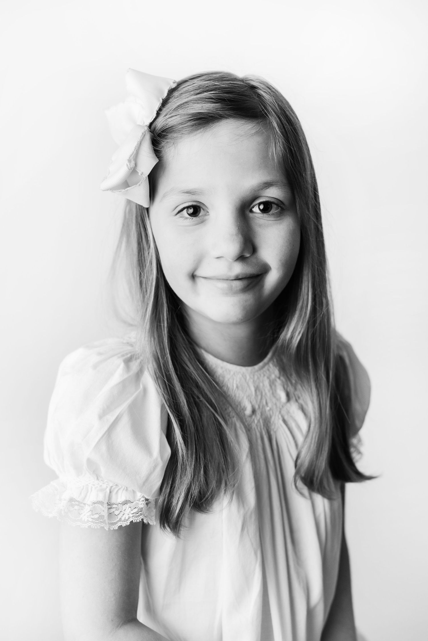 Black and white portrait of young person in white dress with bow in hair.