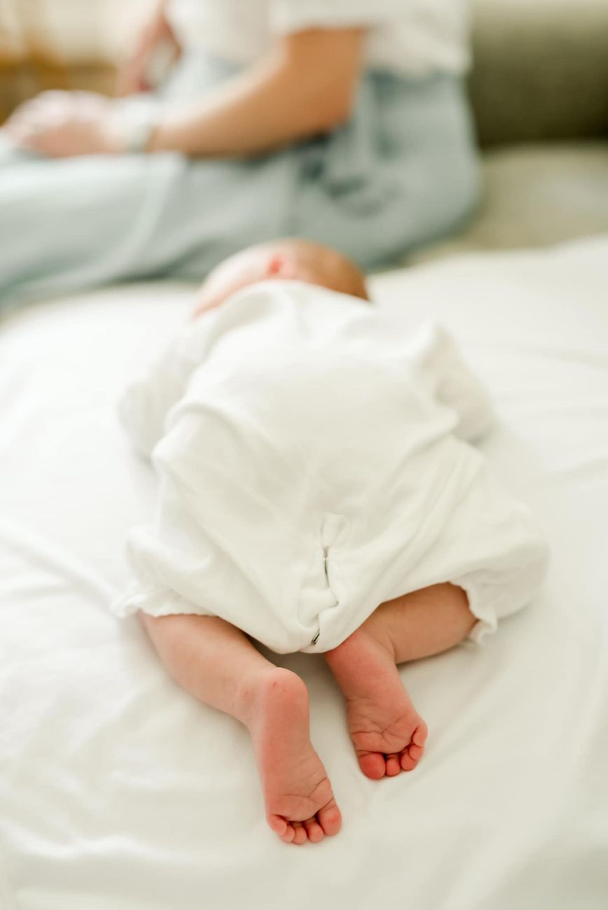Close-up of tiny baby feet peeking out from white blankets in soft natural light.