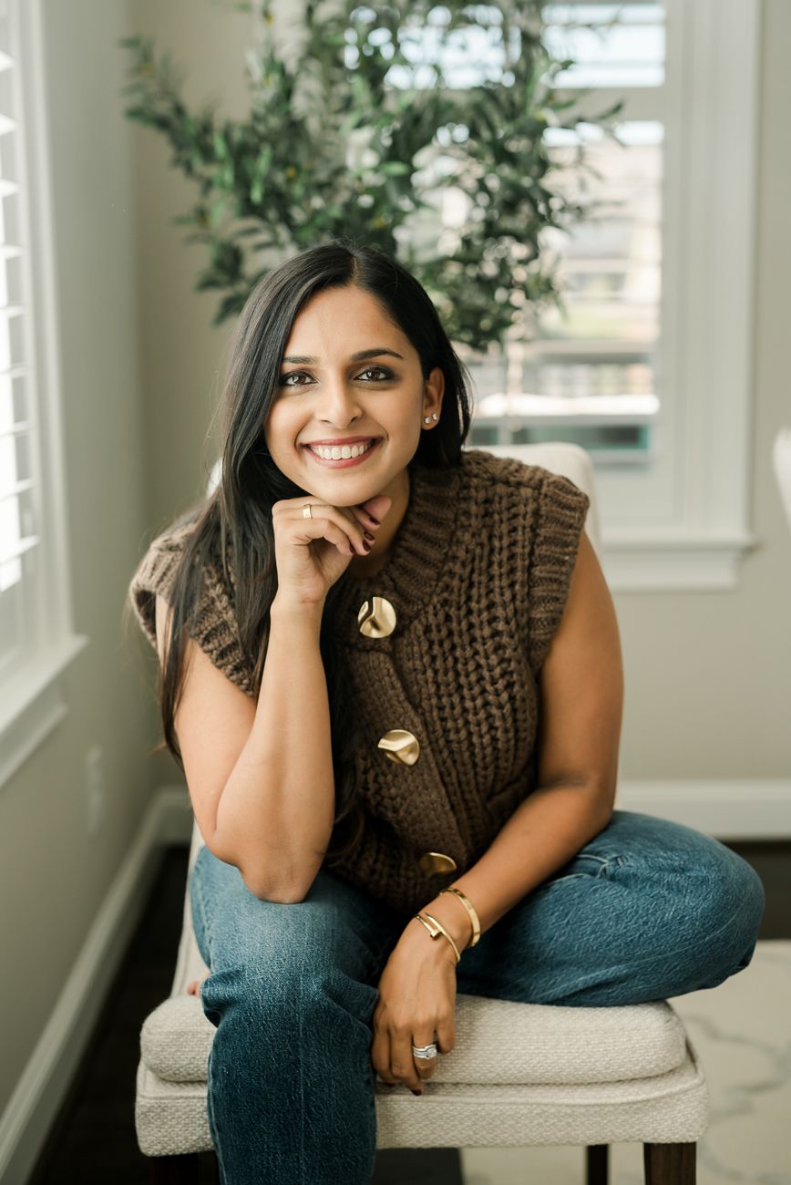 Person in brown sweater and jeans relaxing on light colored couch.