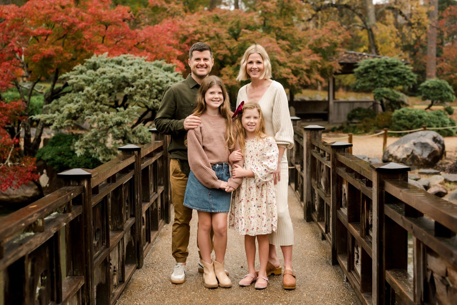 Family of four posing on wooden bridge with autumn foliage in background.