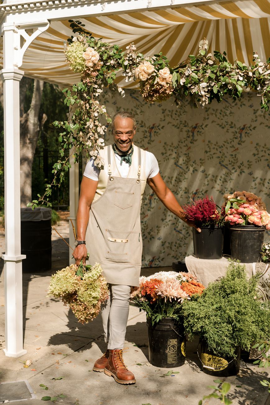 Florist working with fresh flowers under a striped canopy at an outdoor event.