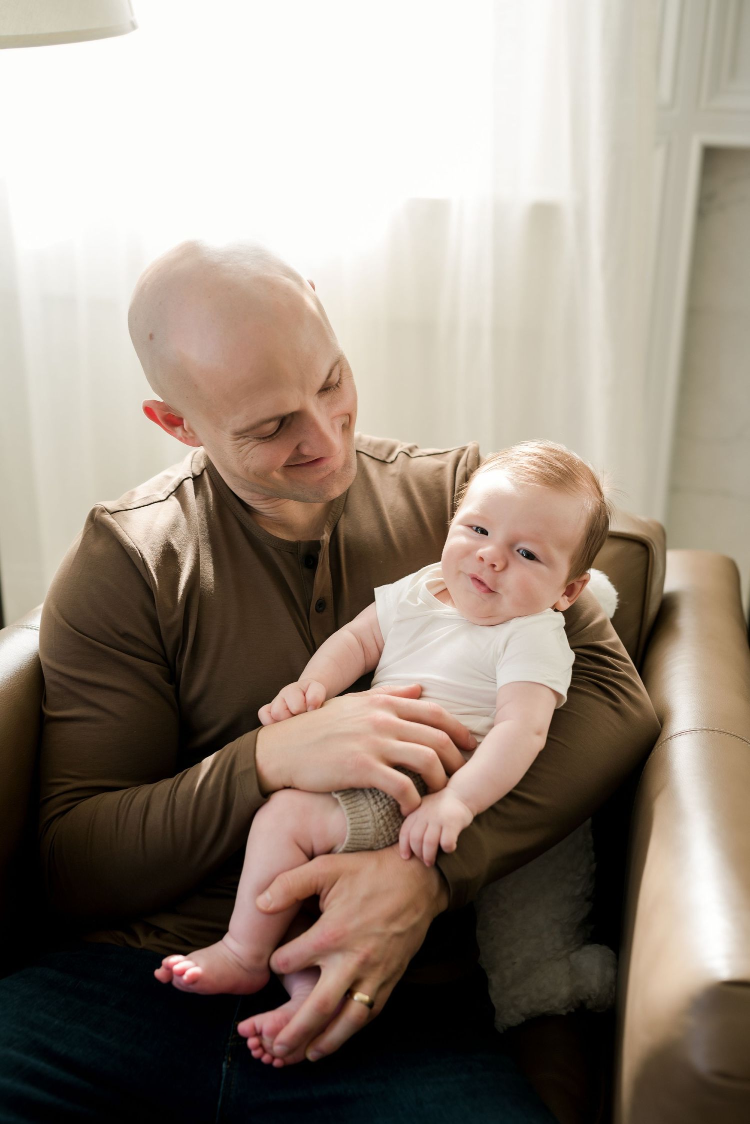 Father holds infant on leather couch in living room.