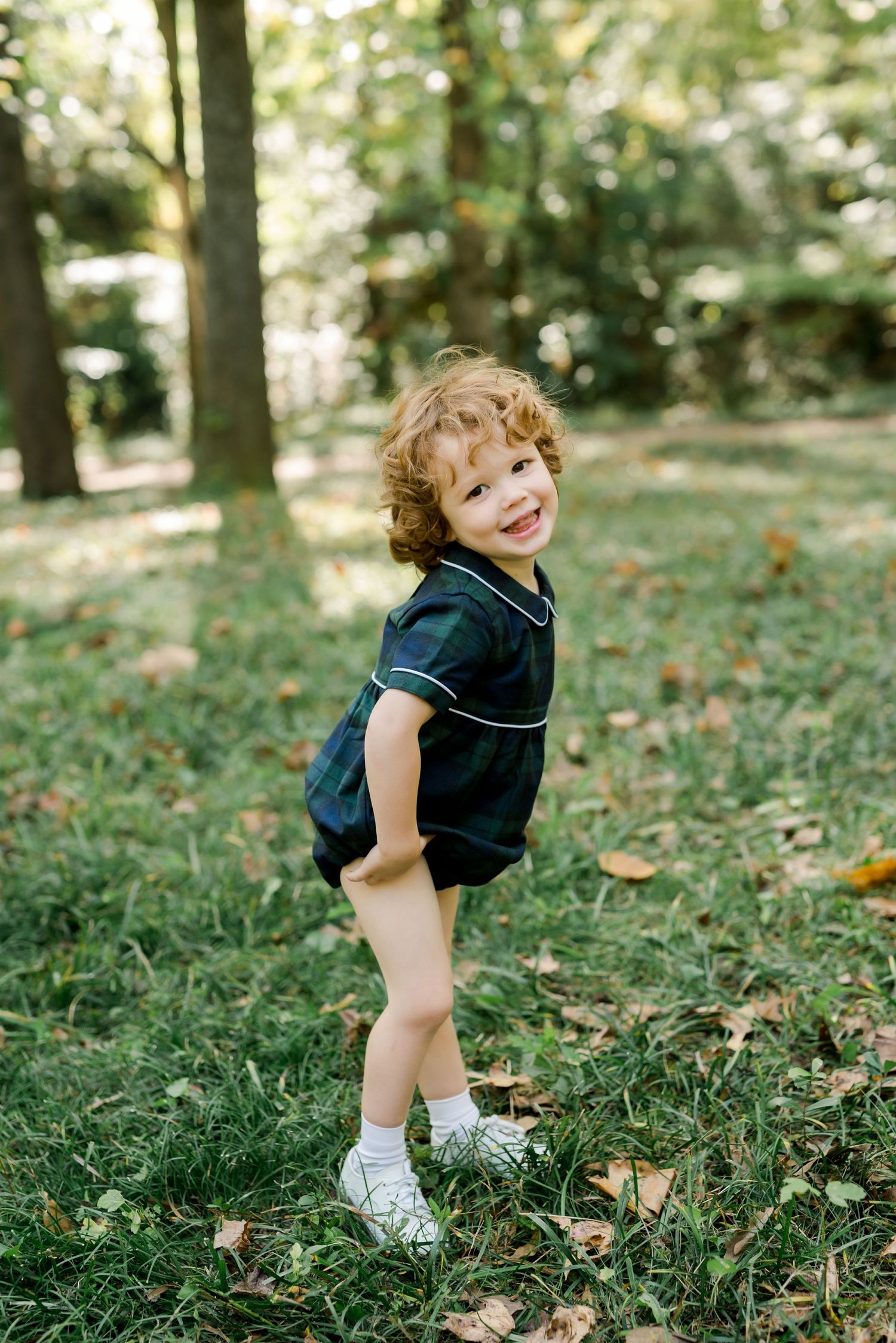 Small child in navy outfit strikes playful pose while standing on grass with autumn leaves.