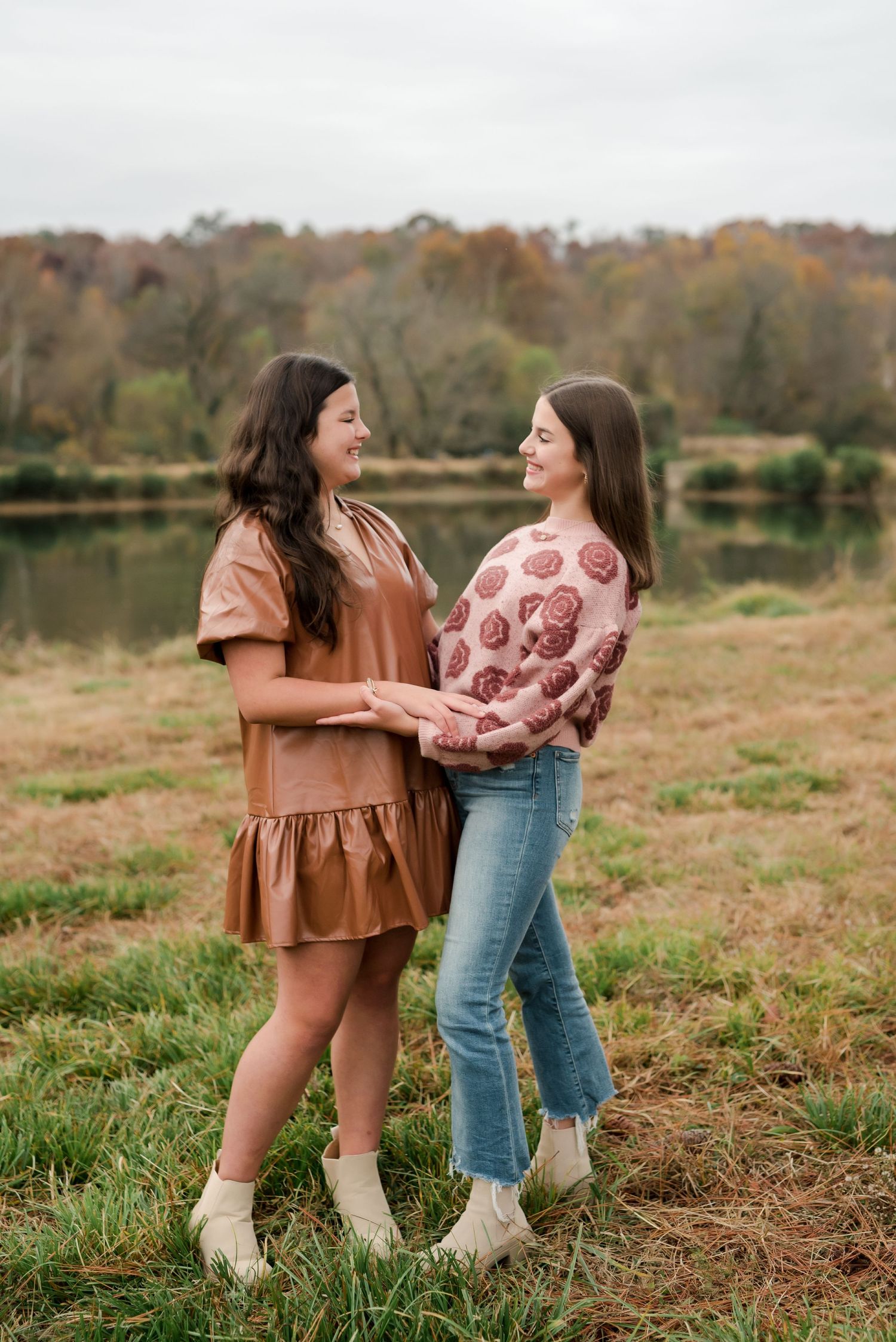Two people in stylish fall outfits share a joyful moment by a lakeside during autumn.