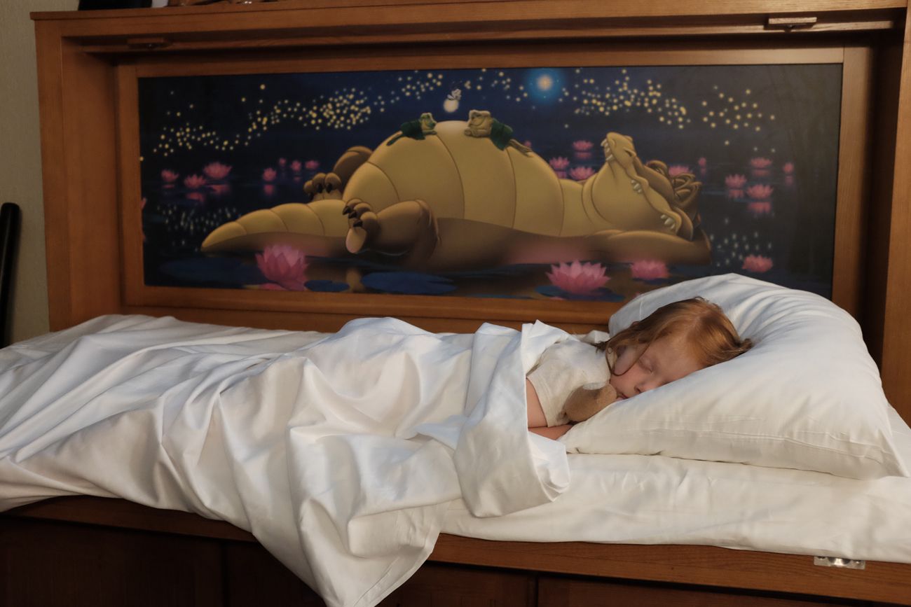 Person sleeping peacefully in hotel room bed with decorative headboard artwork.