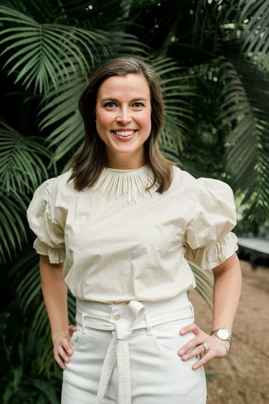 Woman in cream colored puff sleeve blouse poses against tropical palm background.