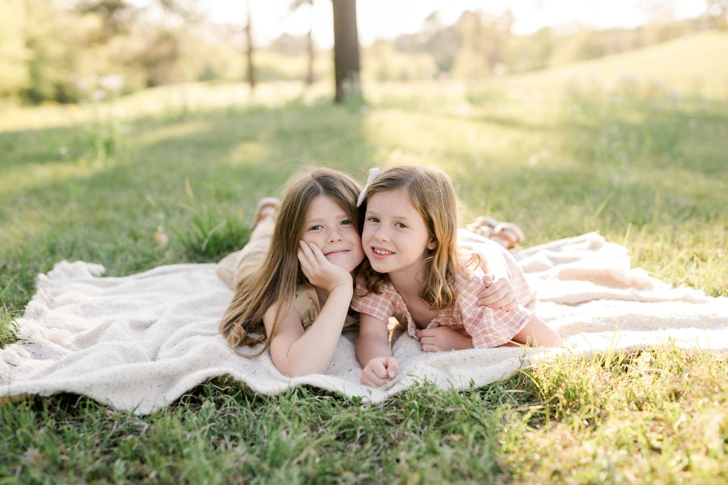 Two people relaxing together on a white blanket in a sunny park setting.