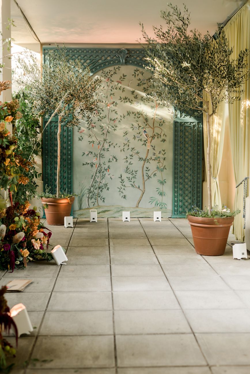 Indoor event space with tiled floor, draped walls, and potted plants for decoration.
