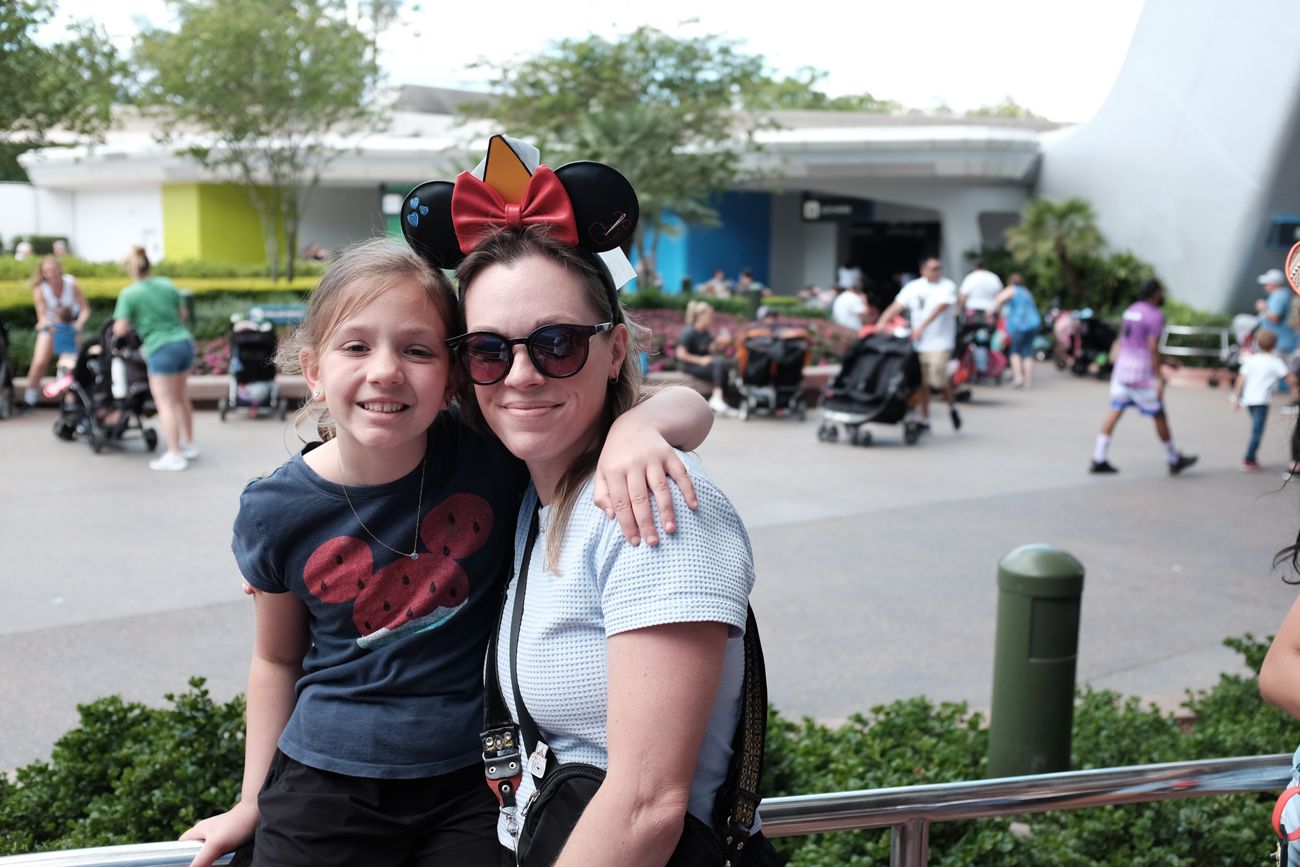 Two theme park visitors wearing Mickey ears pose together outdoors.