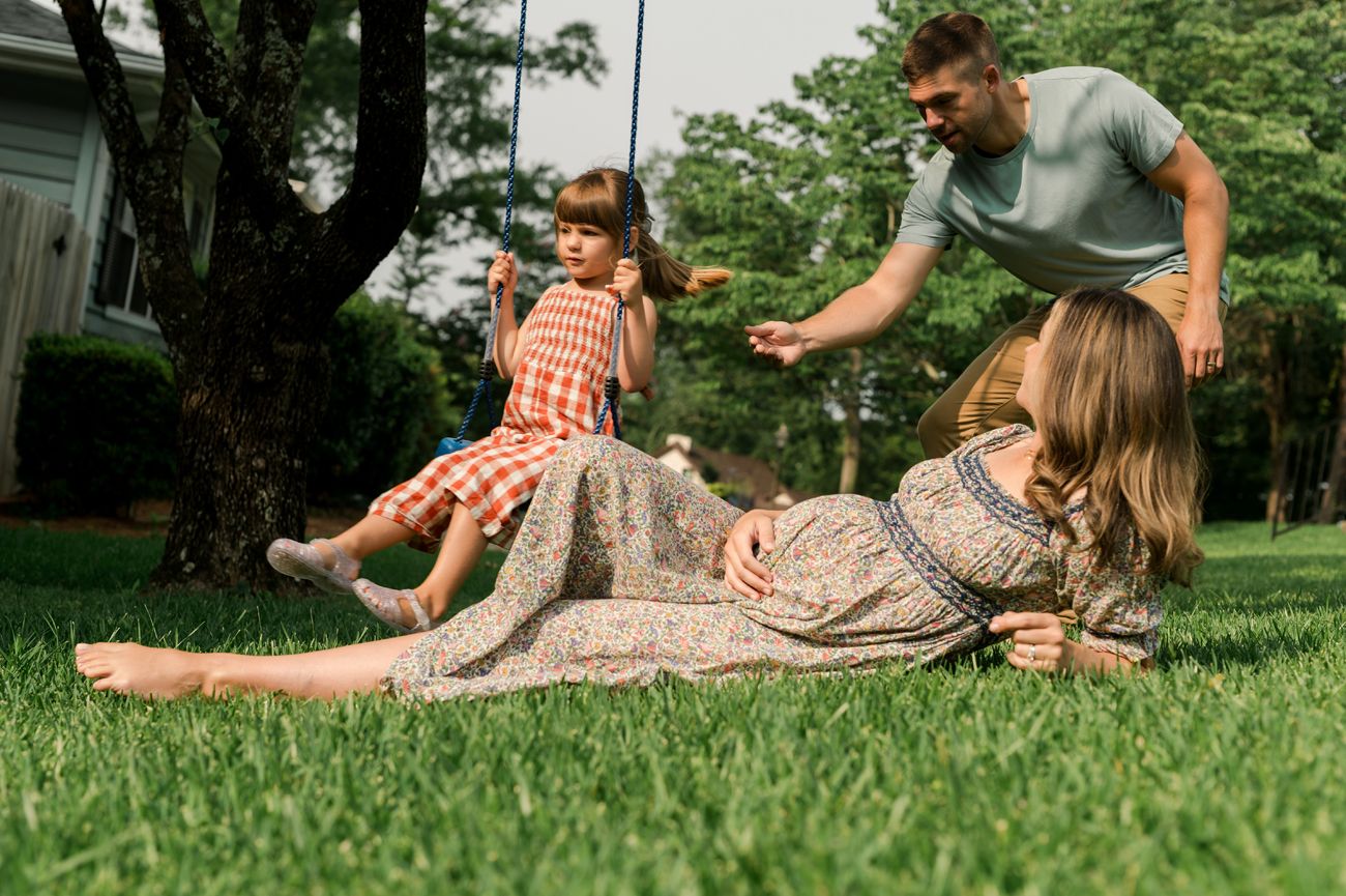 Family playing outdoors on green grass, dad and two young girls enjoying a sunny day in a lush backyard.