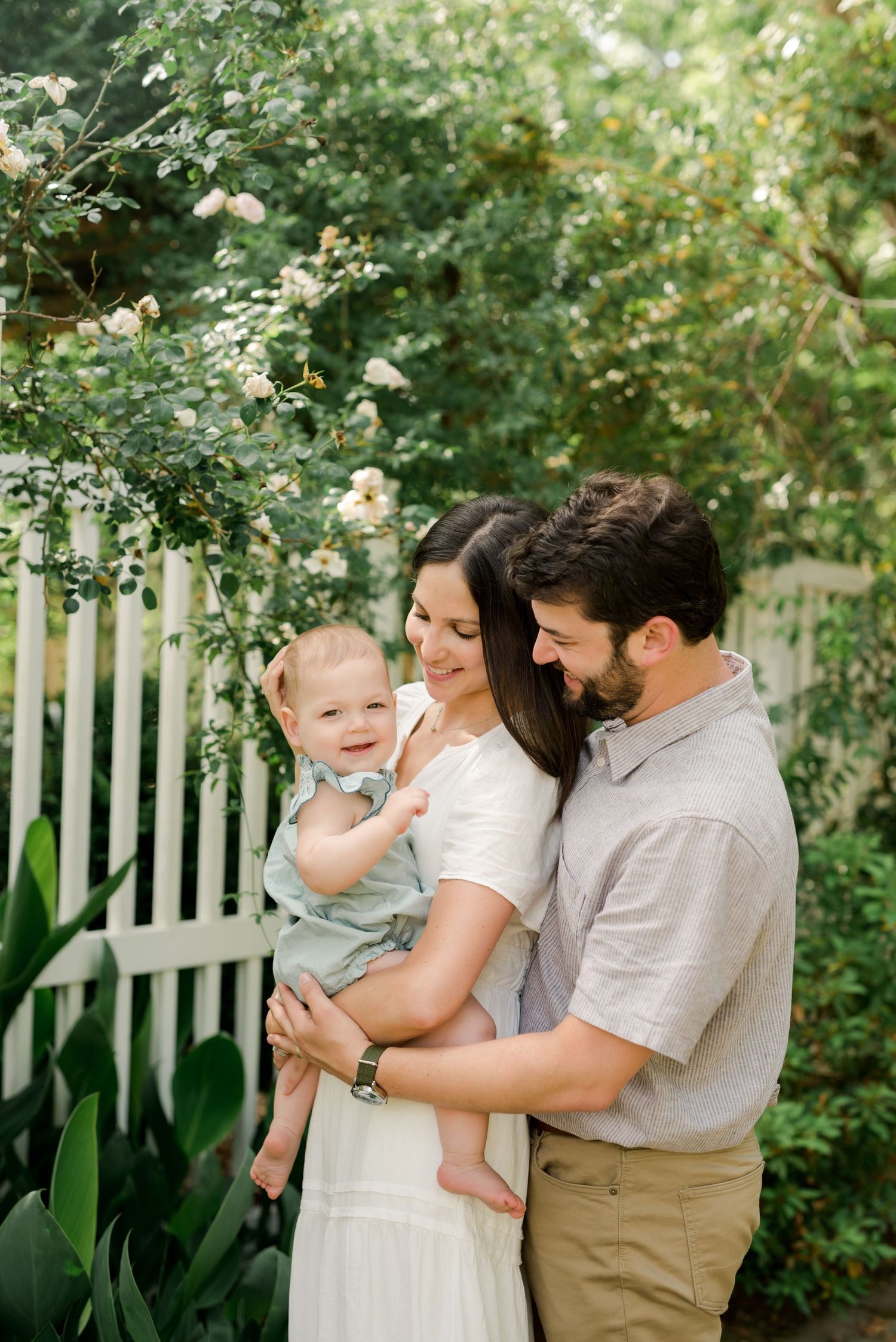Family sharing joyful moment together in garden with white picket fence and flowering bushes.