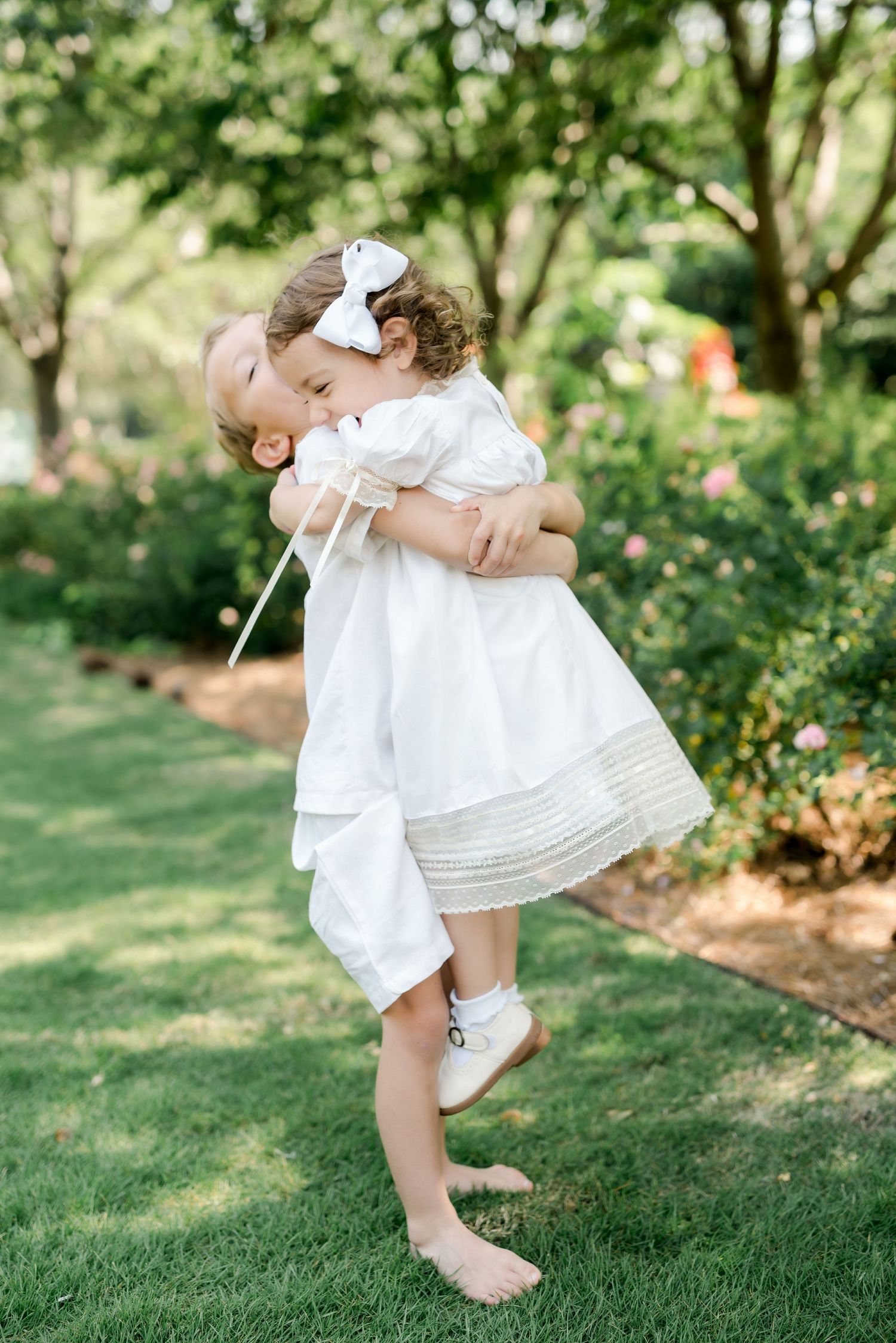 A sweet moment of play and laughter captured between siblings in matching white outfits in a garden.
