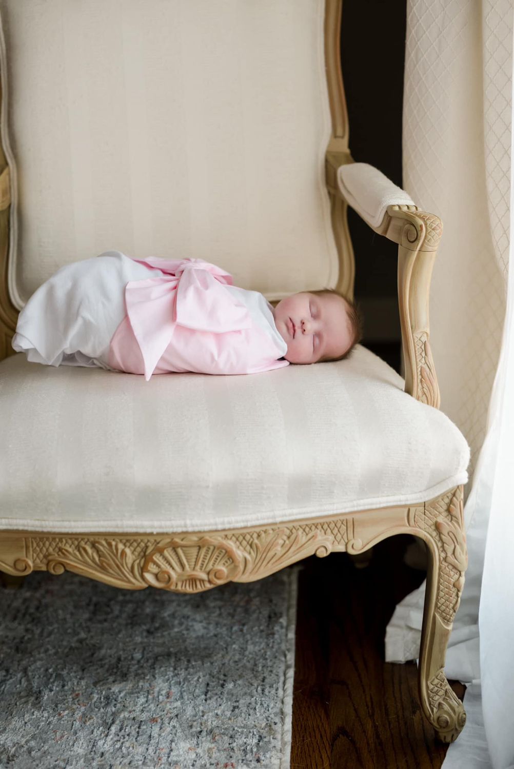 Woman in flowy white dress holding newborn on rustic porch with swing.