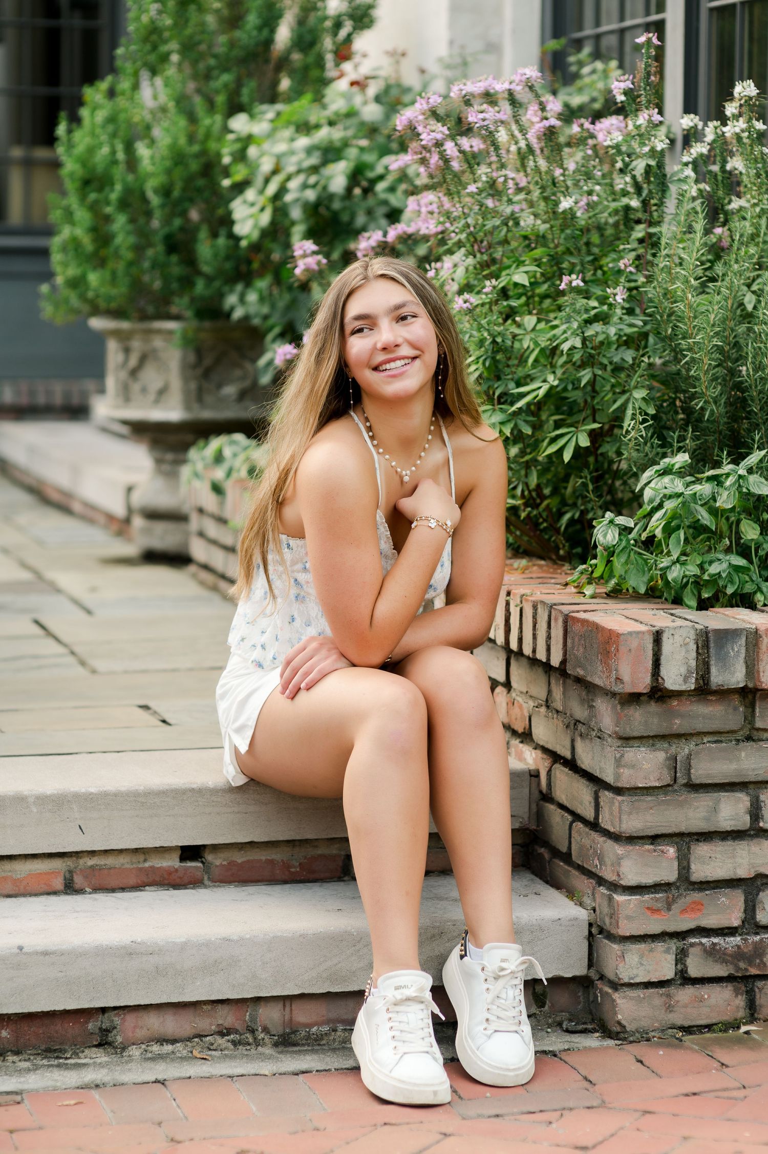 Young person sitting on brick steps surrounded by blooming pink flowers in an outdoor garden setting.