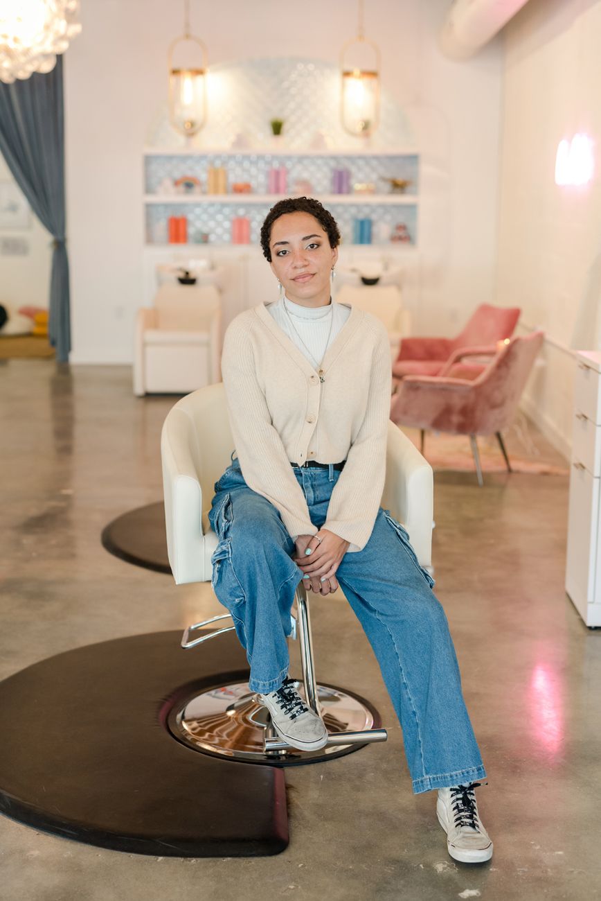 Person in casual attire sitting on salon chair in modern retail space.