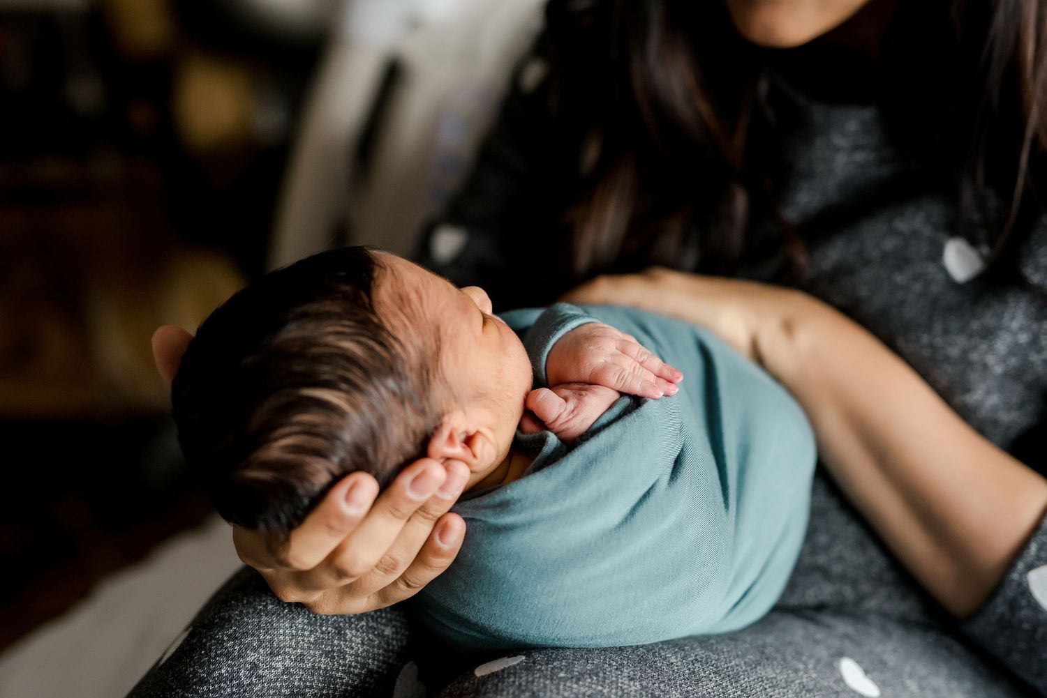 A close-up shot of gentle hands holding a sleeping newborn baby wrapped in blue.