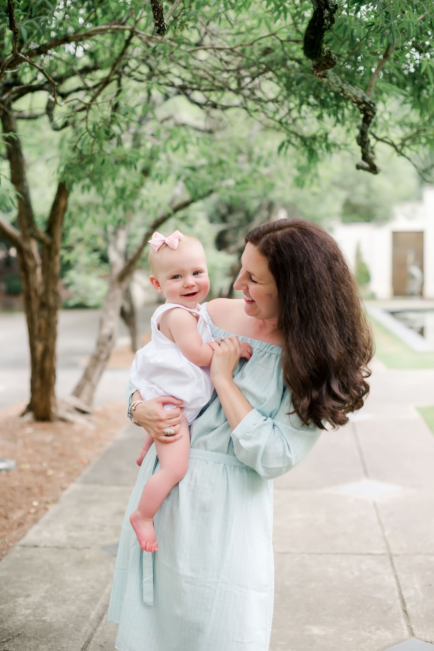Mother and baby share a joyful moment together under green trees in a garden setting.