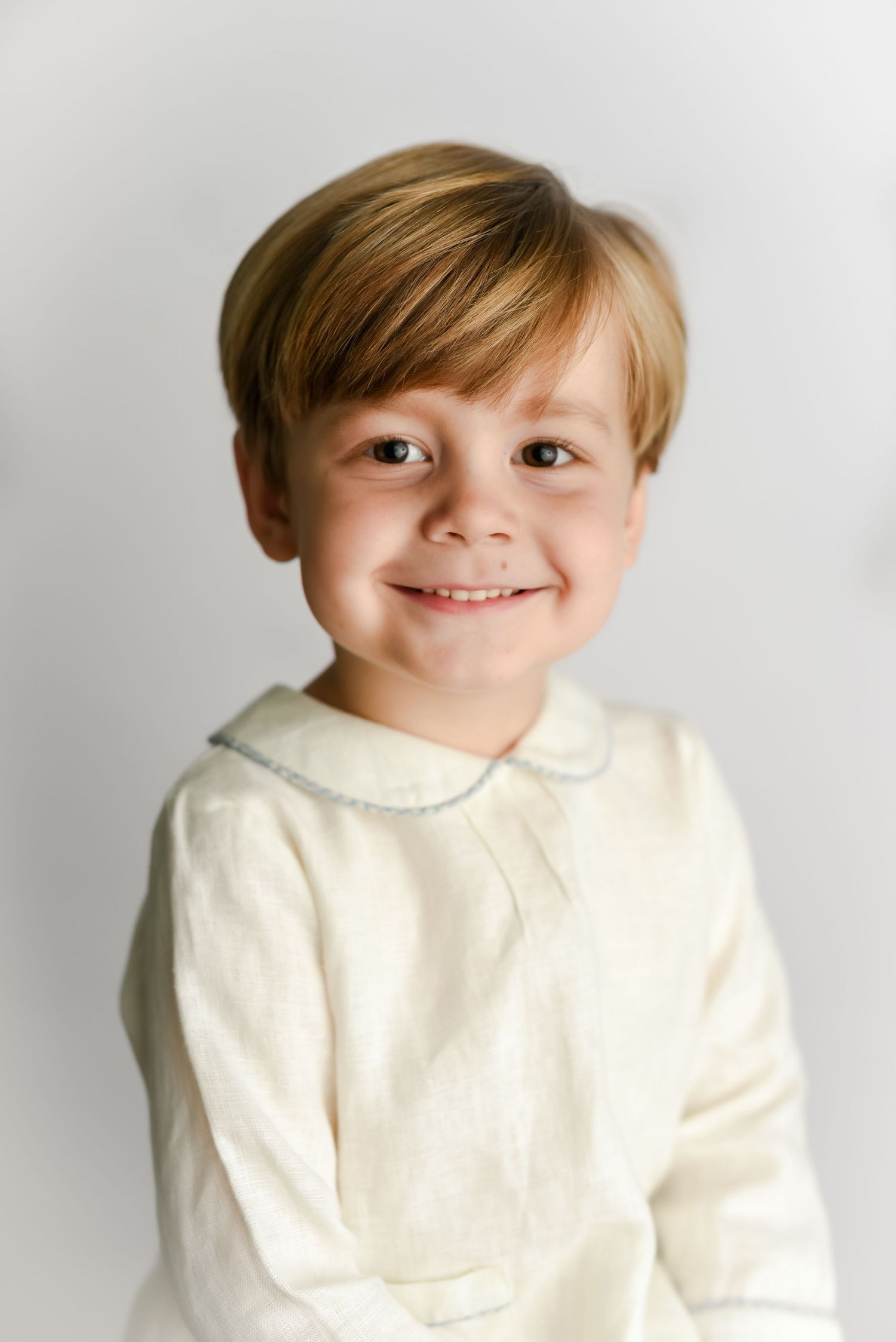 Child with short hair wearing cream collared shirt smiles warmly at camera.