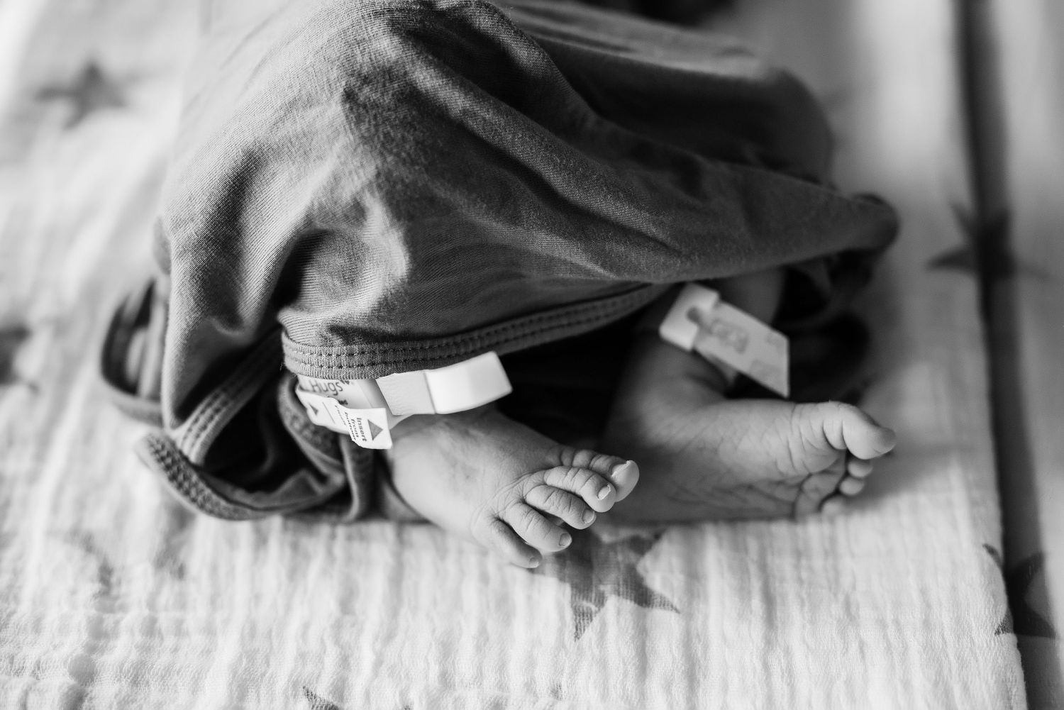 Black and white image showing tiny newborn feet with hospital identification bracelet.