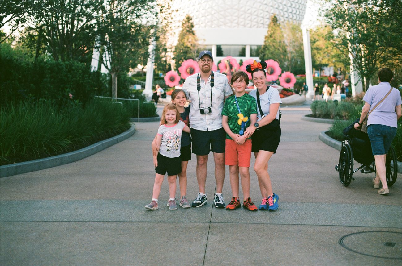 A group of visitors posing on a pathway at Disney World with balloons and souvenirs.