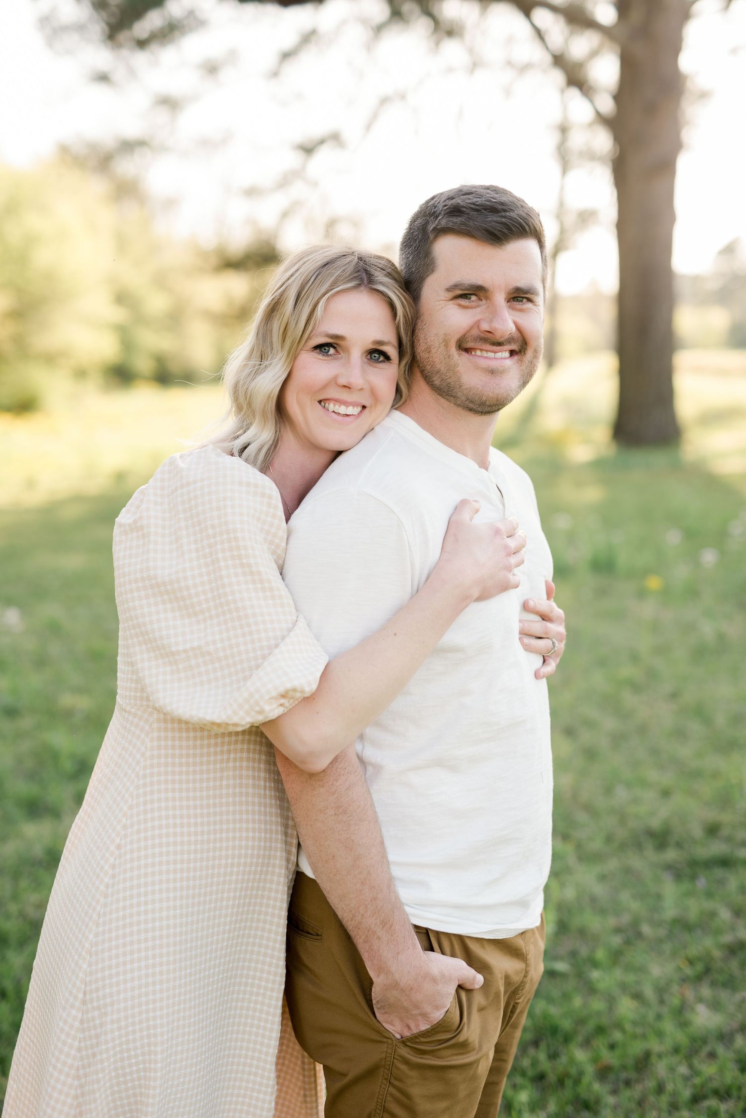 Loving couple in coordinating cream outfits embracing outdoors during golden hour.