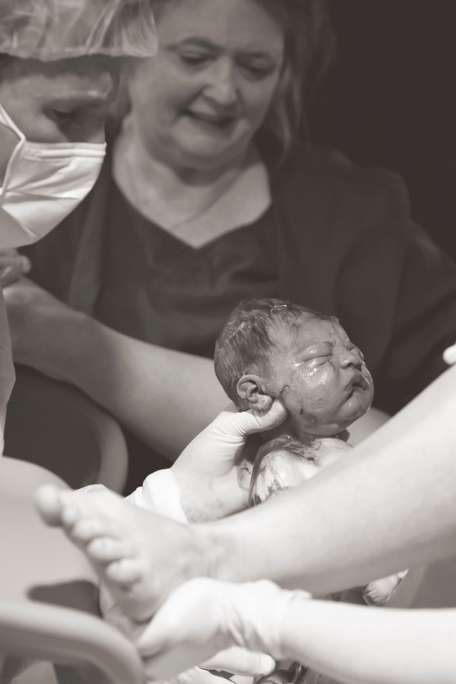 Black and white photo capturing the first moments after birth of a newborn baby.