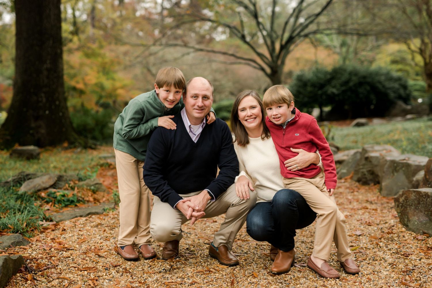 Family of four poses together on a leaf-covered path during fall season.
