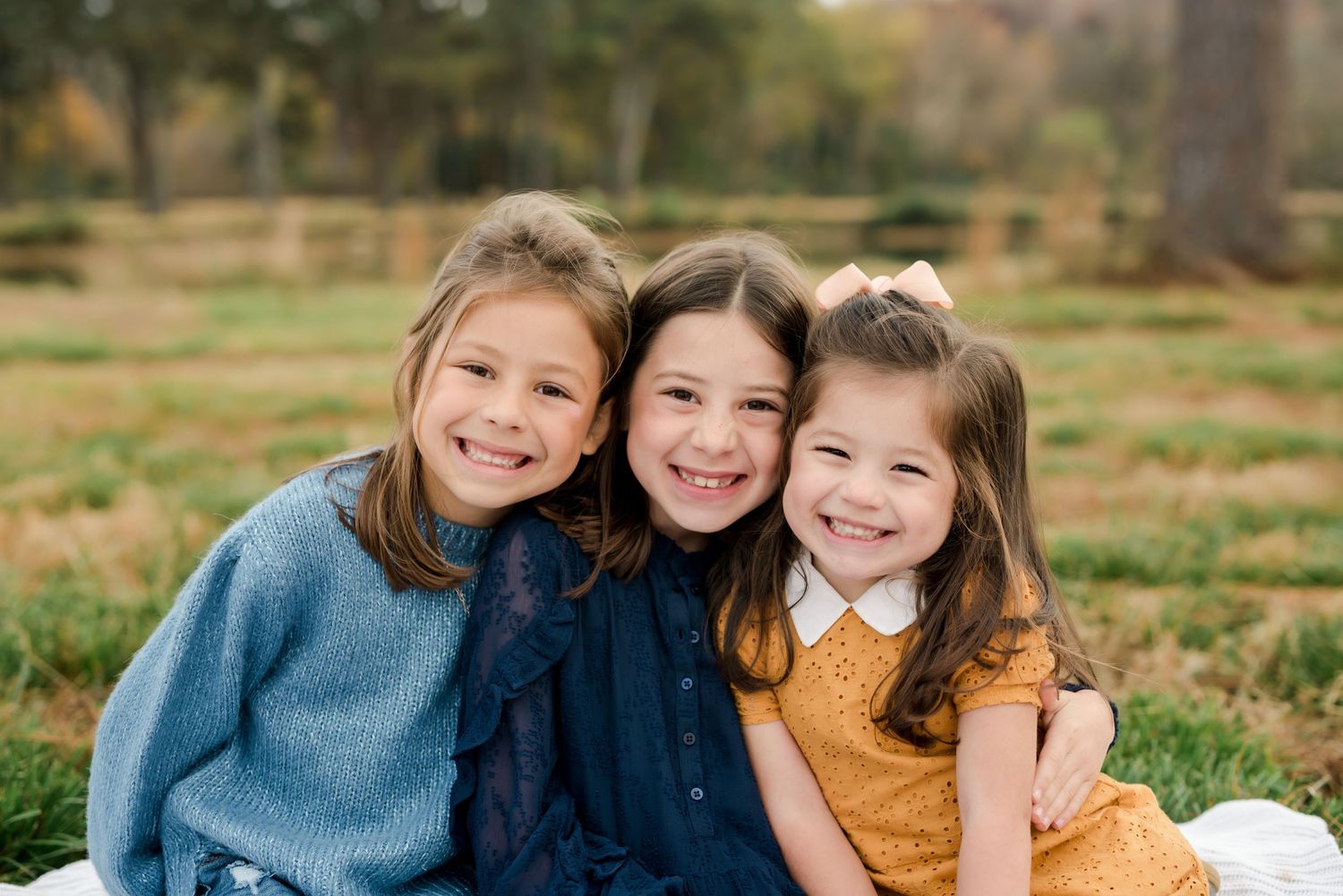 Three young friends in cozy sweaters share warm embraces during an autumn outdoor photoshoot.