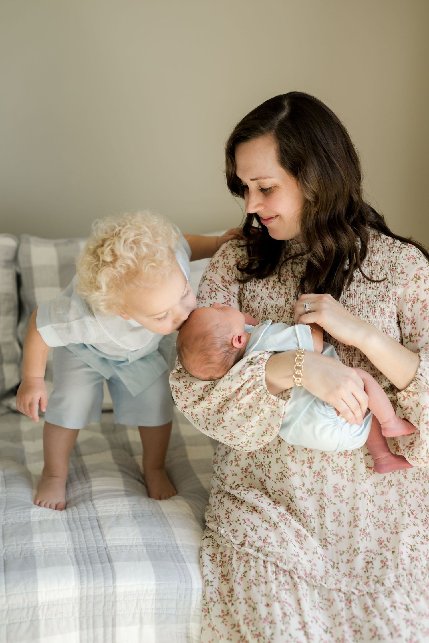 Family moment on a bed featuring a woman in floral dress with young children.