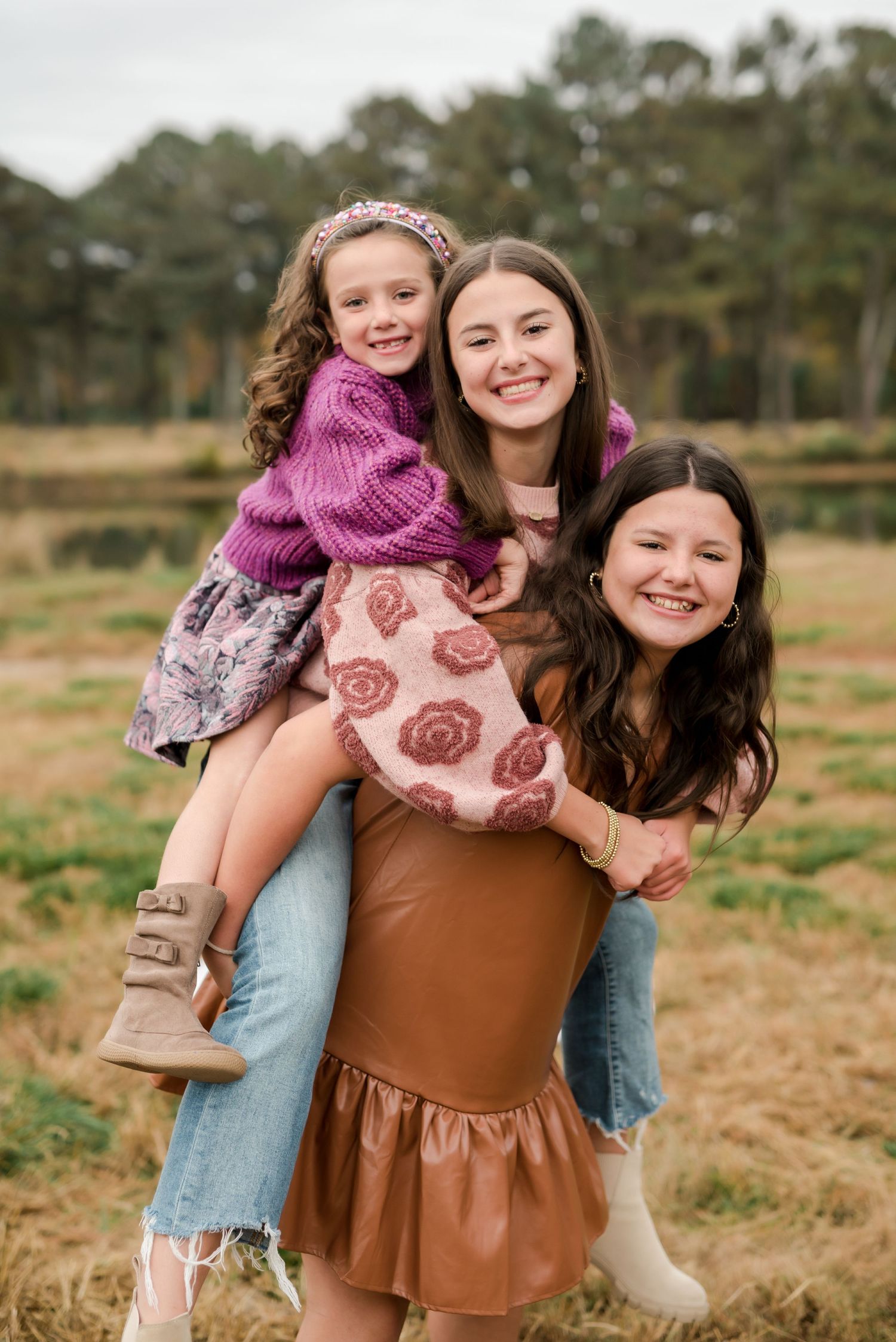 Three people hugging and smiling in casual fall outfits outdoors with pine trees in background.