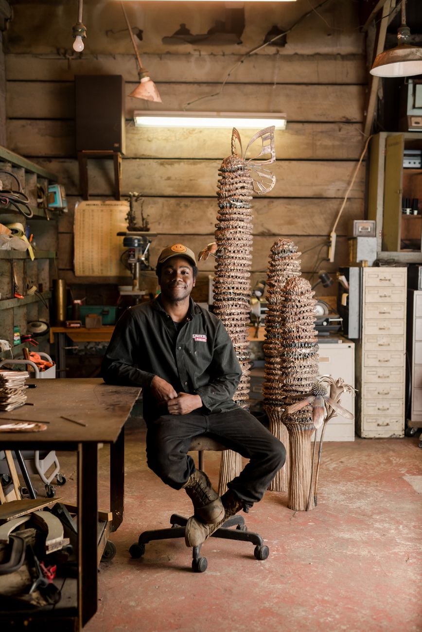 Craftsperson sitting in workshop with metal sculptures.