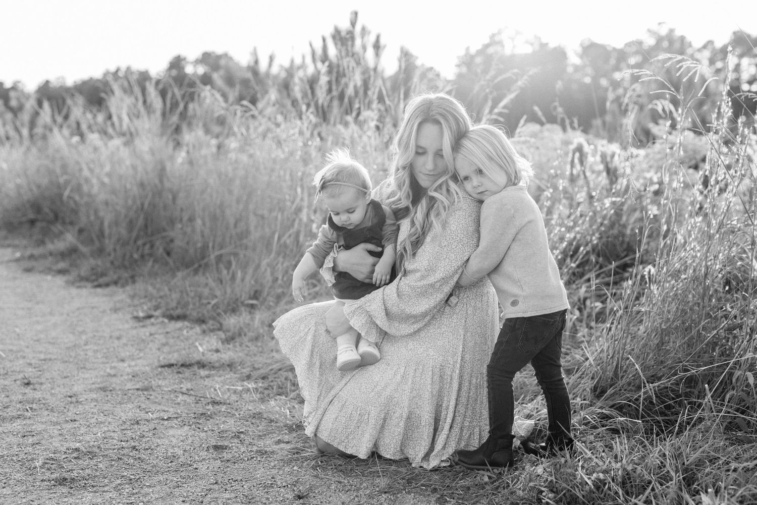 Black and white image of family embracing outdoors among tall grasses.
