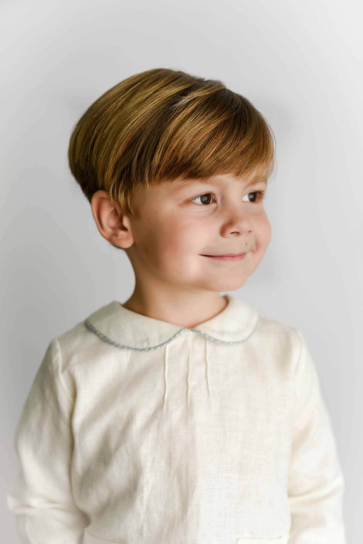 Portrait of child in cream collared shirt with styled hair against light background.