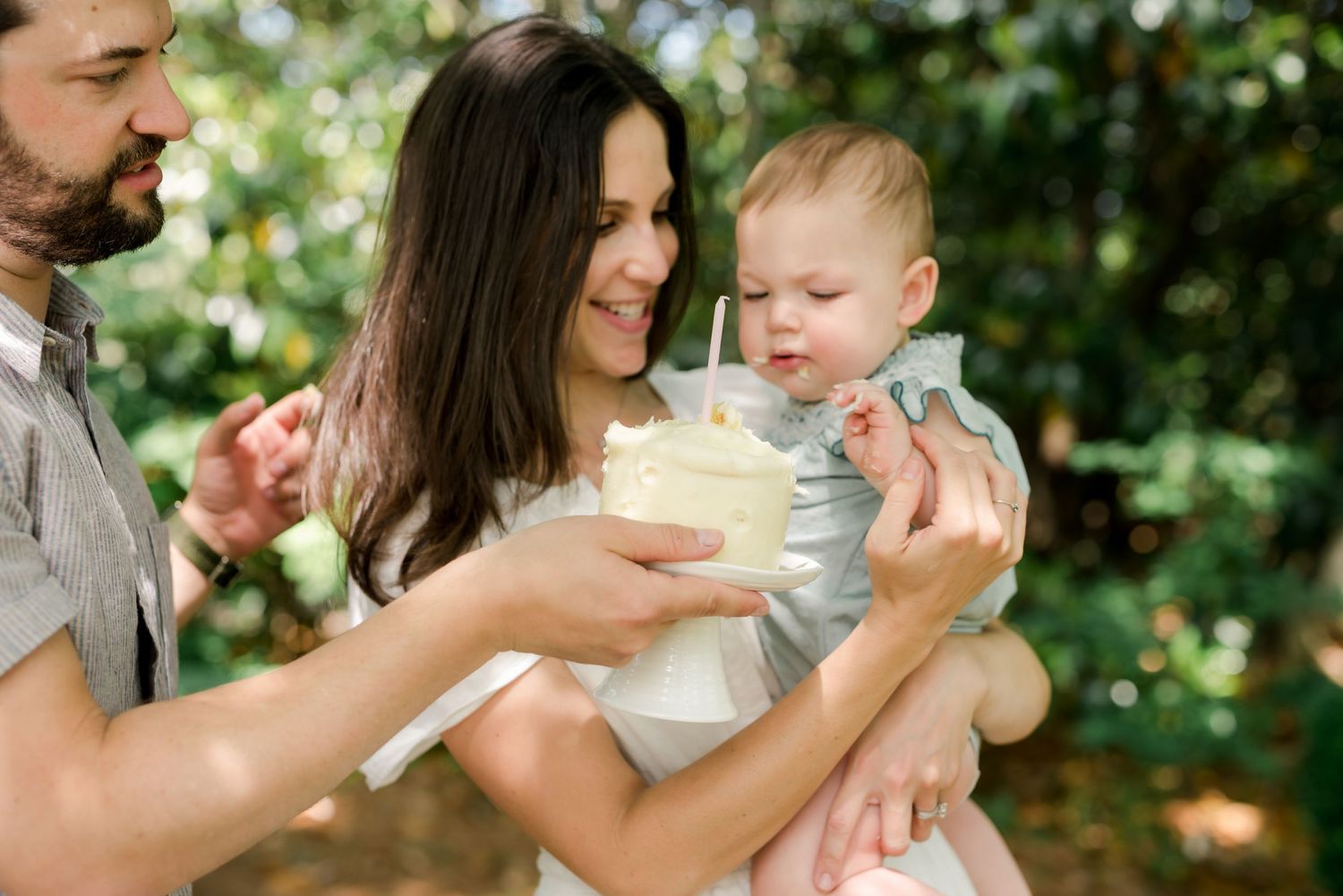 Parents sharing joyful moment with baby outdoors in garden setting.