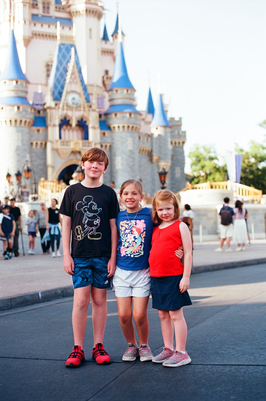 Three young visitors posing in front of Cinderella Castle at Magic Kingdom.
