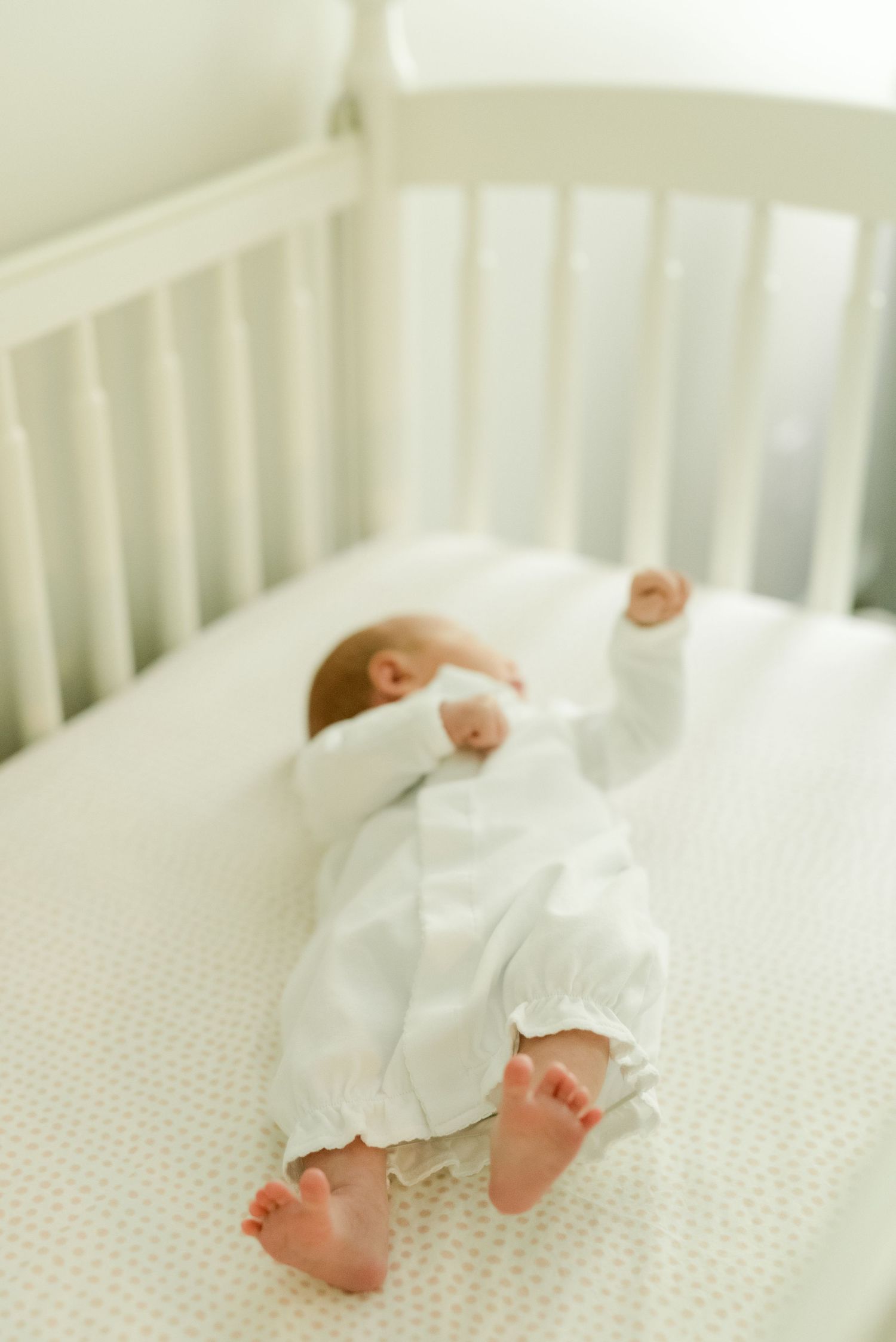 A sleeping infant wearing white clothing lies peacefully in a white crib.