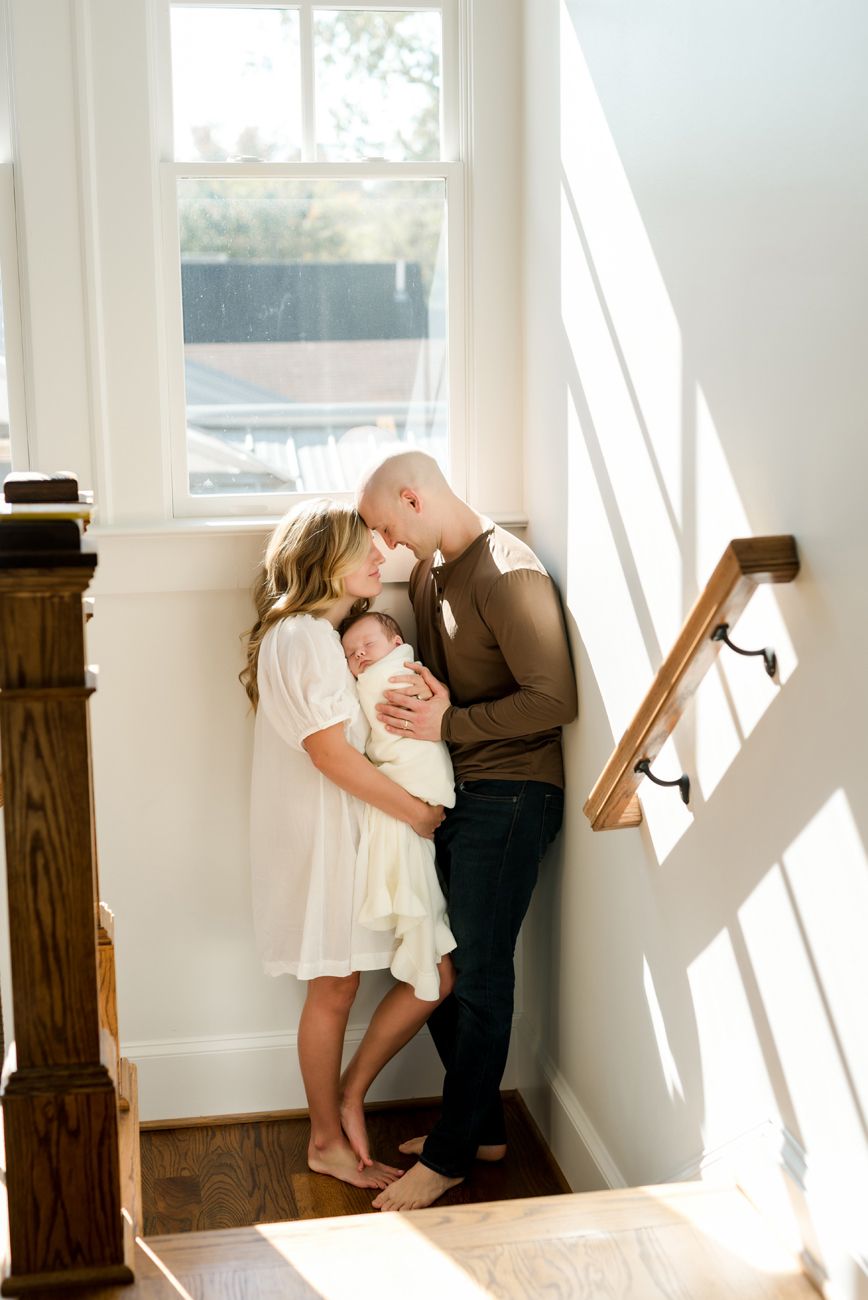 A tender moment captured in a bright sunlit hallway with white walls and wooden accents.