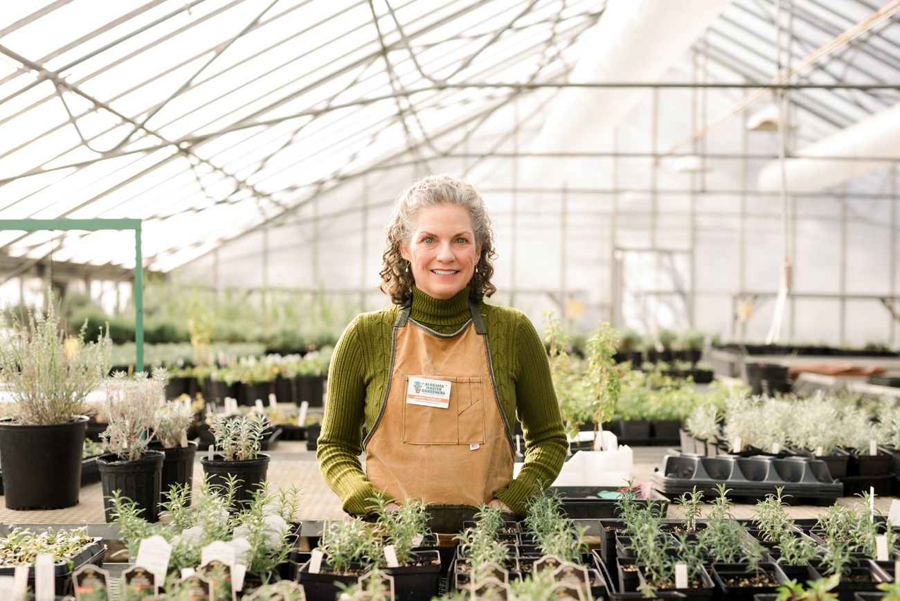 Person working in large greenhouse with rows of plants visible.